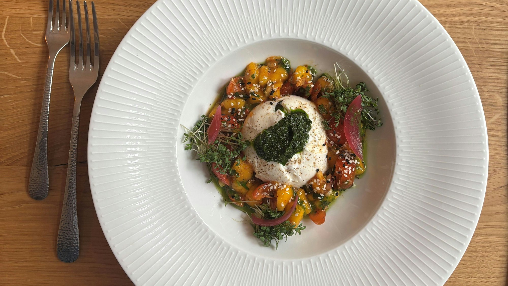 Das Bild zeigt das Gericht auf einem weißen Teller, daneben zwei Gabeln.