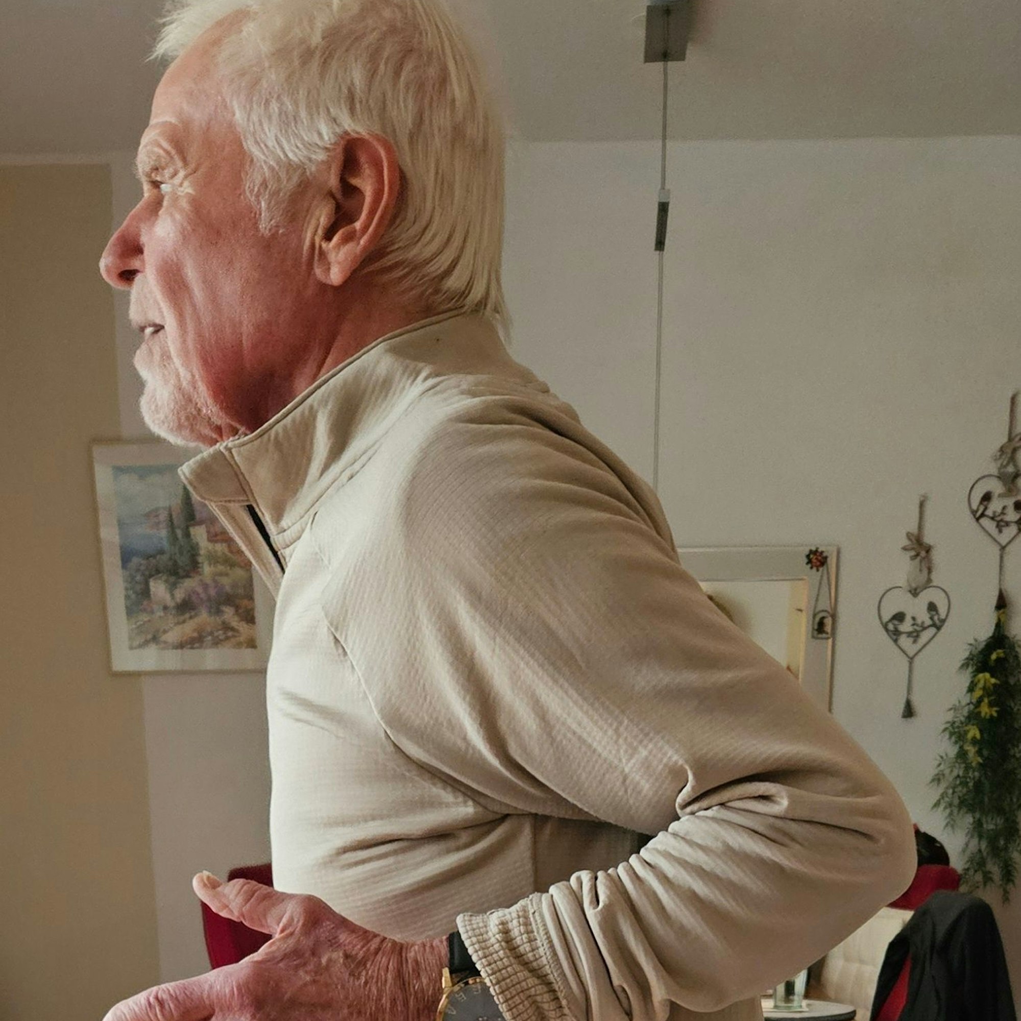 Ein Senior im Gymnastikdress führt die Ellenbogen hinter dem Rücken zusammen.