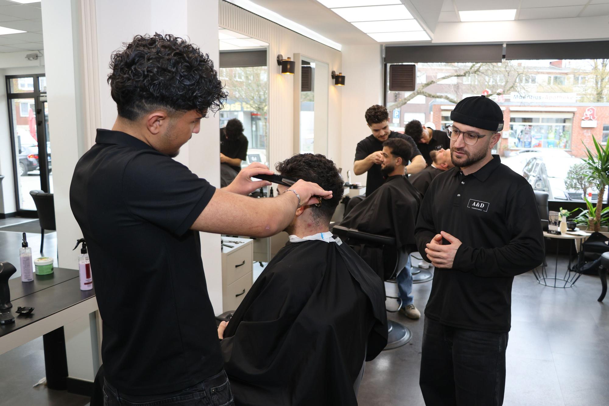 Auf dem Bild sind der Inhaber und Mitarbeiter eines Friseursalons zu sehen.