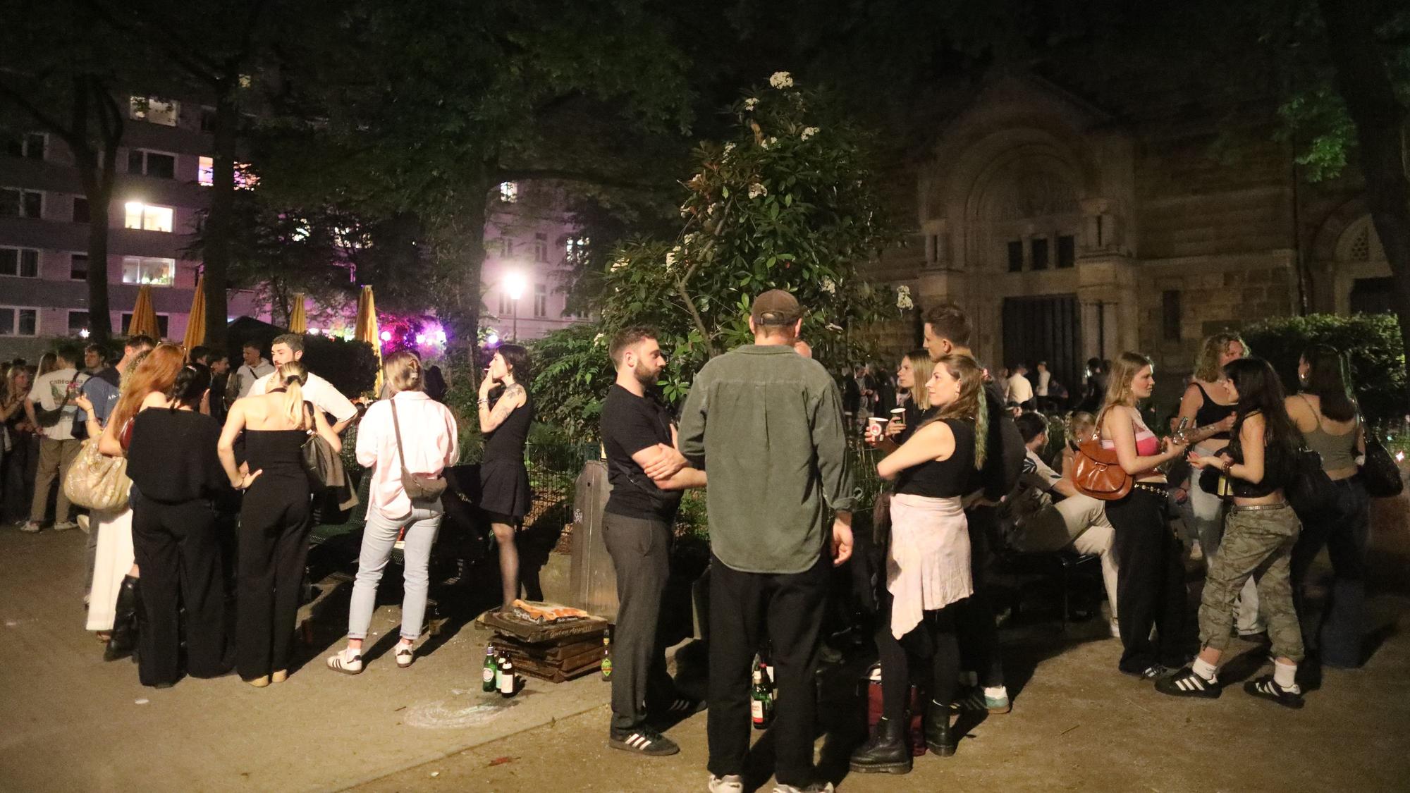 Das Bild zeigt die Situation auf dem Brüsseler Platz im April 2025: Menschen treffen und unterhalten sich, manche halten dabei ein Getränk.