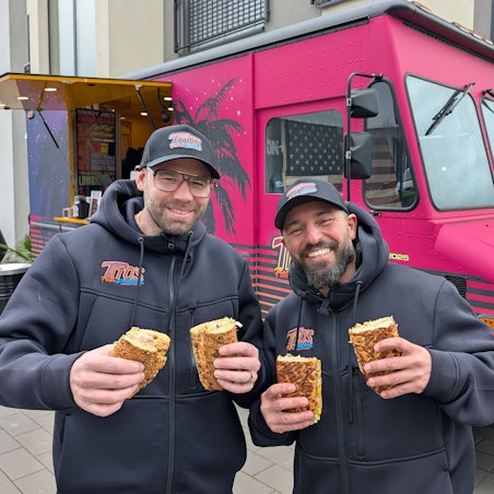 Das Foto zeigt die beiden Betreiber mit Baguettes vor dem Foodtruck.