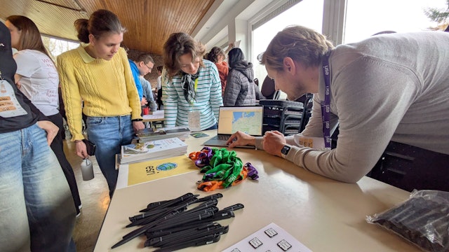 Zwei Frauen und ein Mann schauen während einer Präsentation auf den Bildschirm eines Laptops