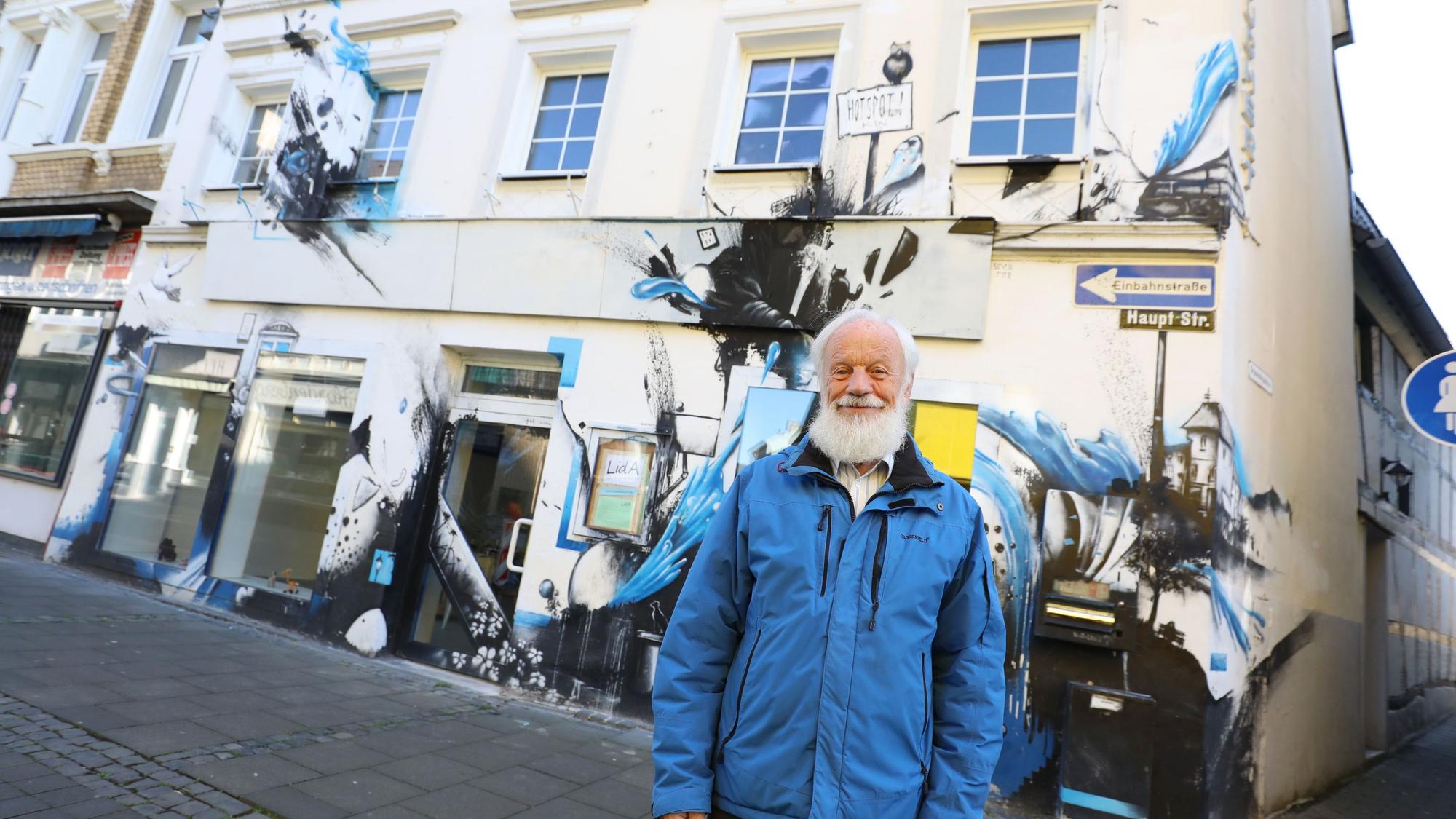 Ein Mann in blauer Jacke vor einem Haus, dessen Fassade mit Graffiti gestaltet ist.