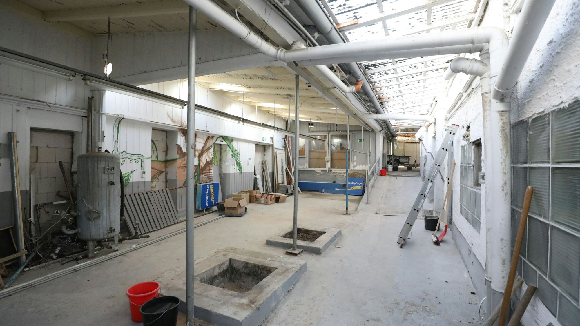 Ein langgezogener Raum mit einer Rampe in der Mitte, an einer Wand lehnen eine Leiter sowie Besen und Schaufel.