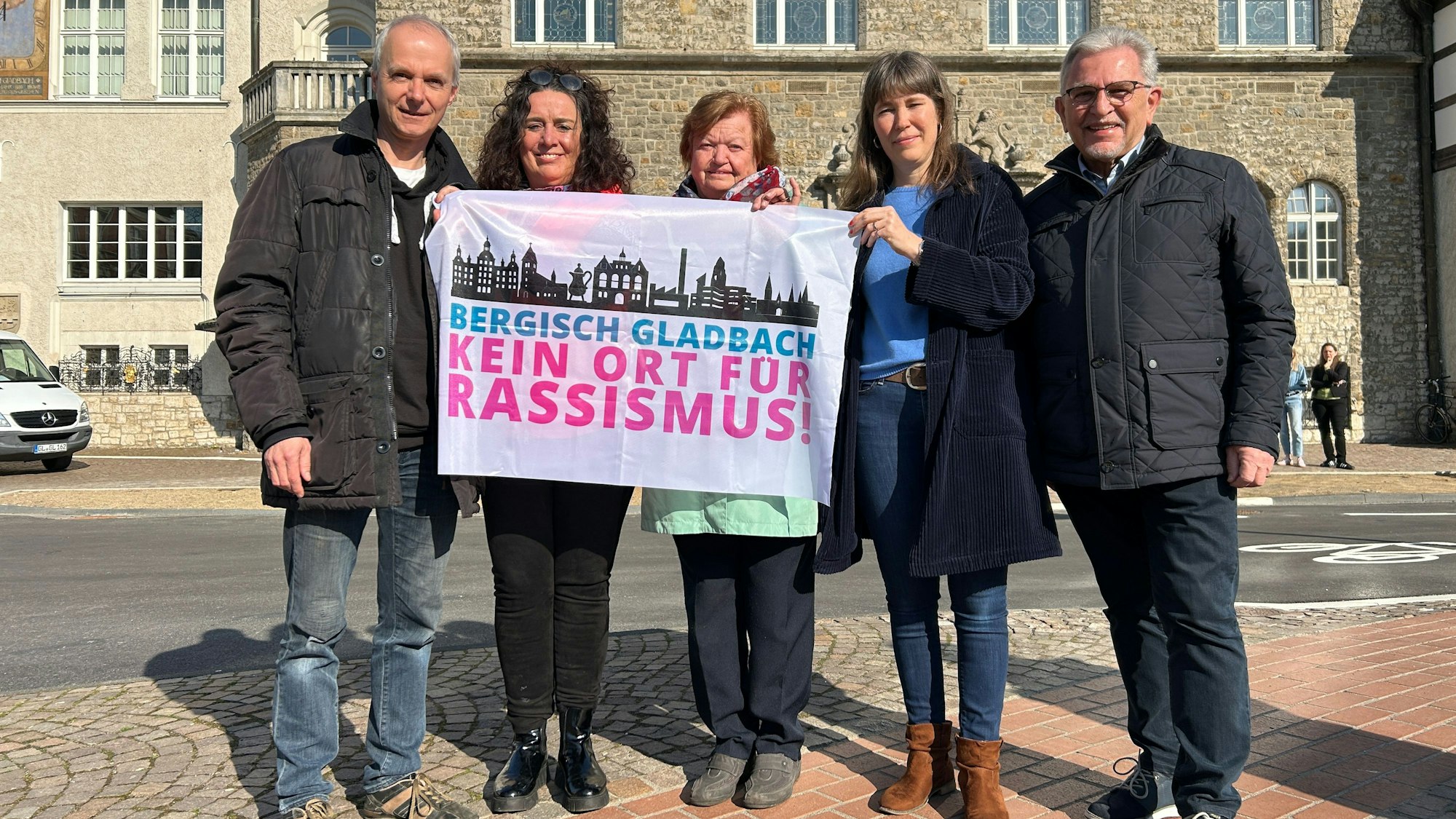 Fünf Personen halten eine Fahne hoch auf der „Bergisch Gladbach – kein Ort für Rassismus!“ geschrieben steht.