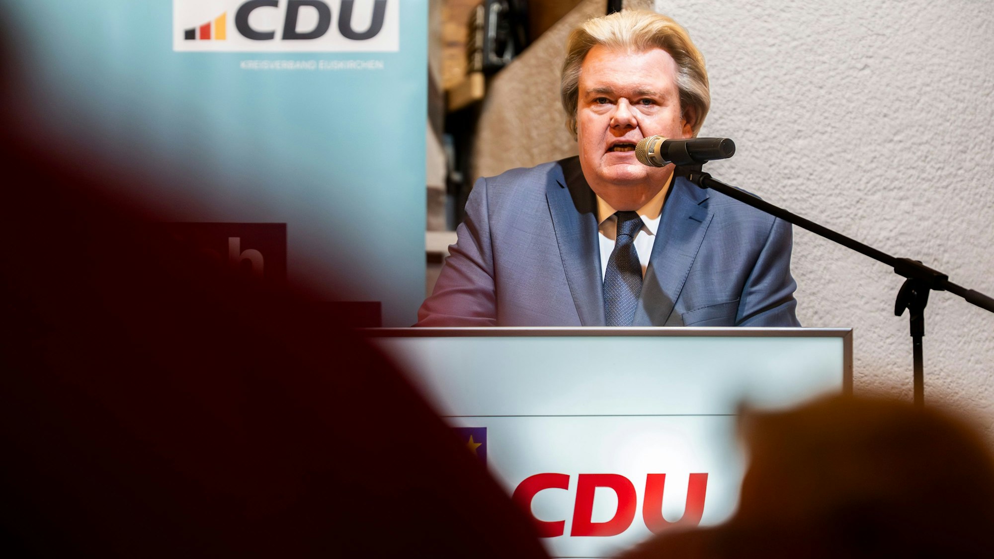 Klaus Voussem steht an einem Rednerpult mit CDU-Logo. Im Vordergrund sind unscharf Menschen im Publikum zu sehen.