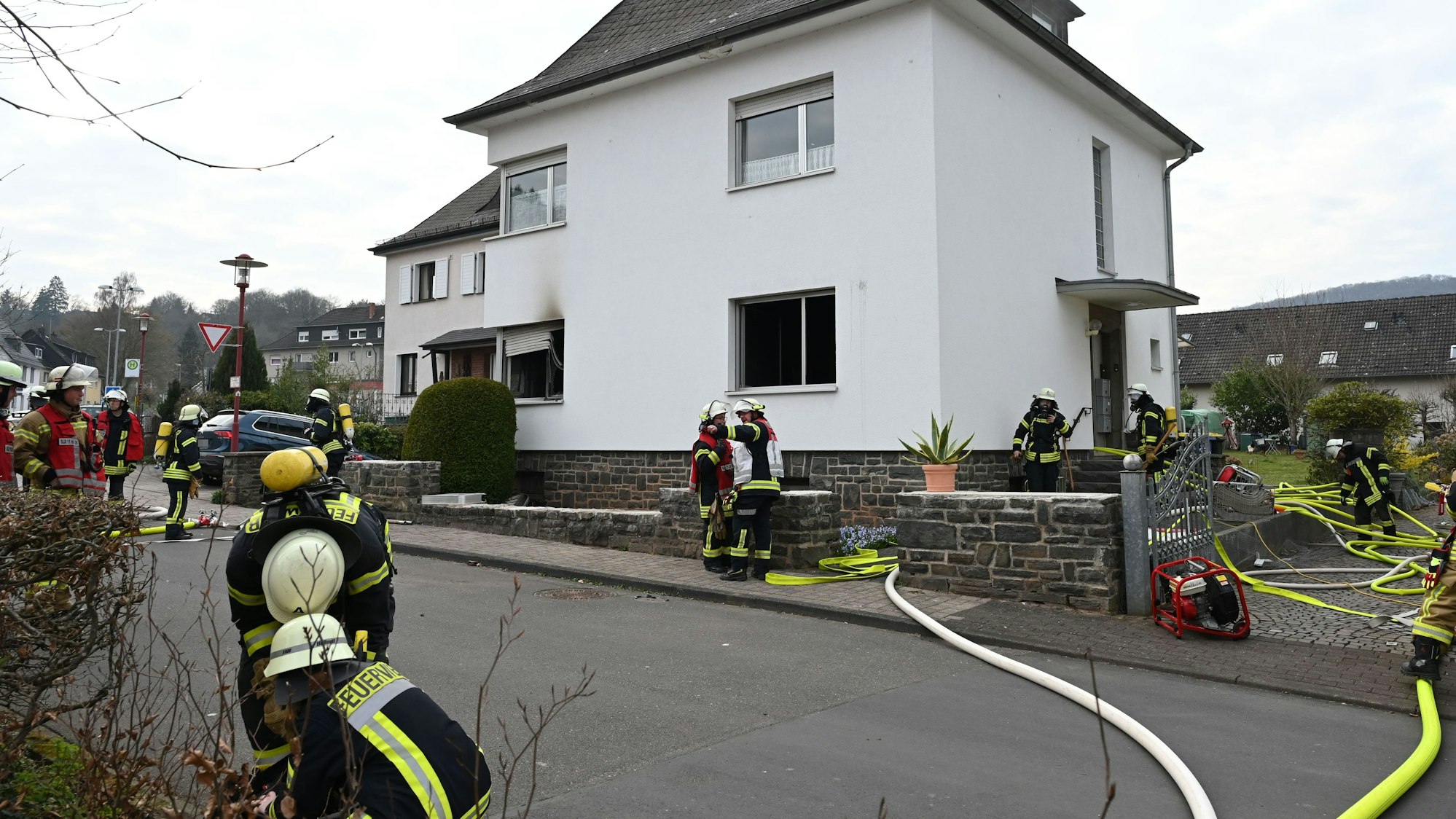Feuerwehrleute haben Schläuche zu einem Haus verlegt. An einem Fenster sind Rauchspuren zu sehen.