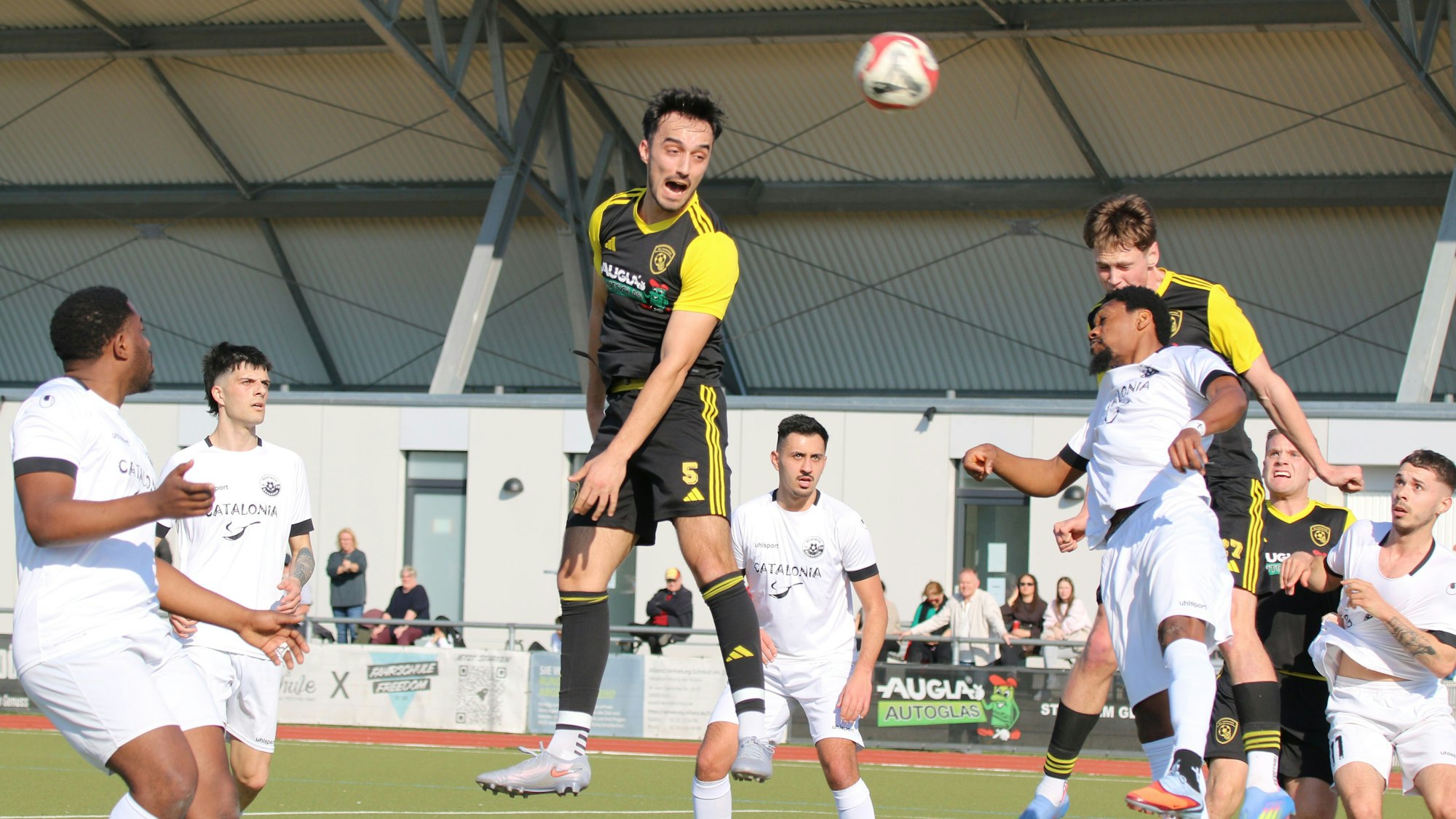 Mehrere Spieler versuchen, den Ball mit dem Kopf zu erreichen, andere beobachten die Szene..