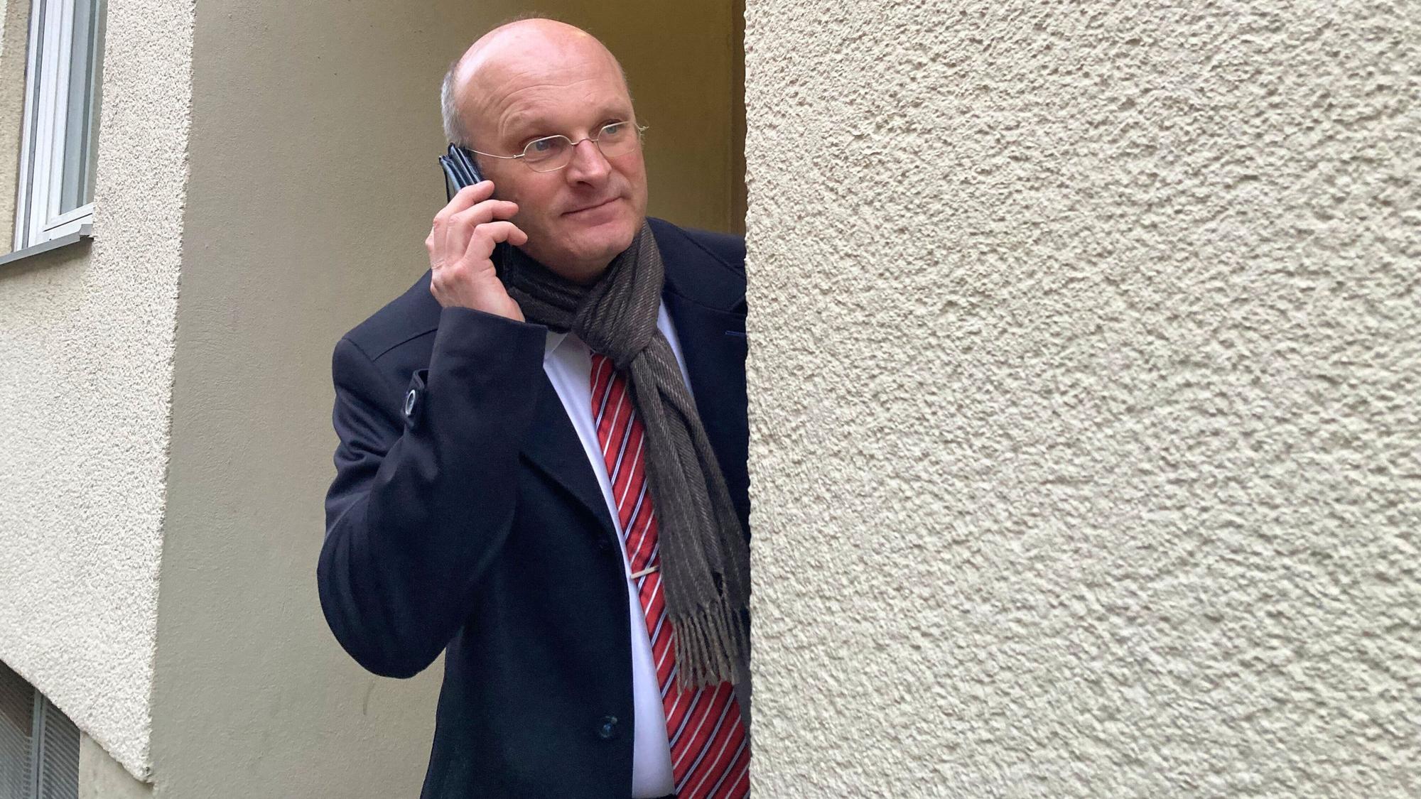 Ein Mann mit einem Handy schaut an einer Hauswand entlang.
