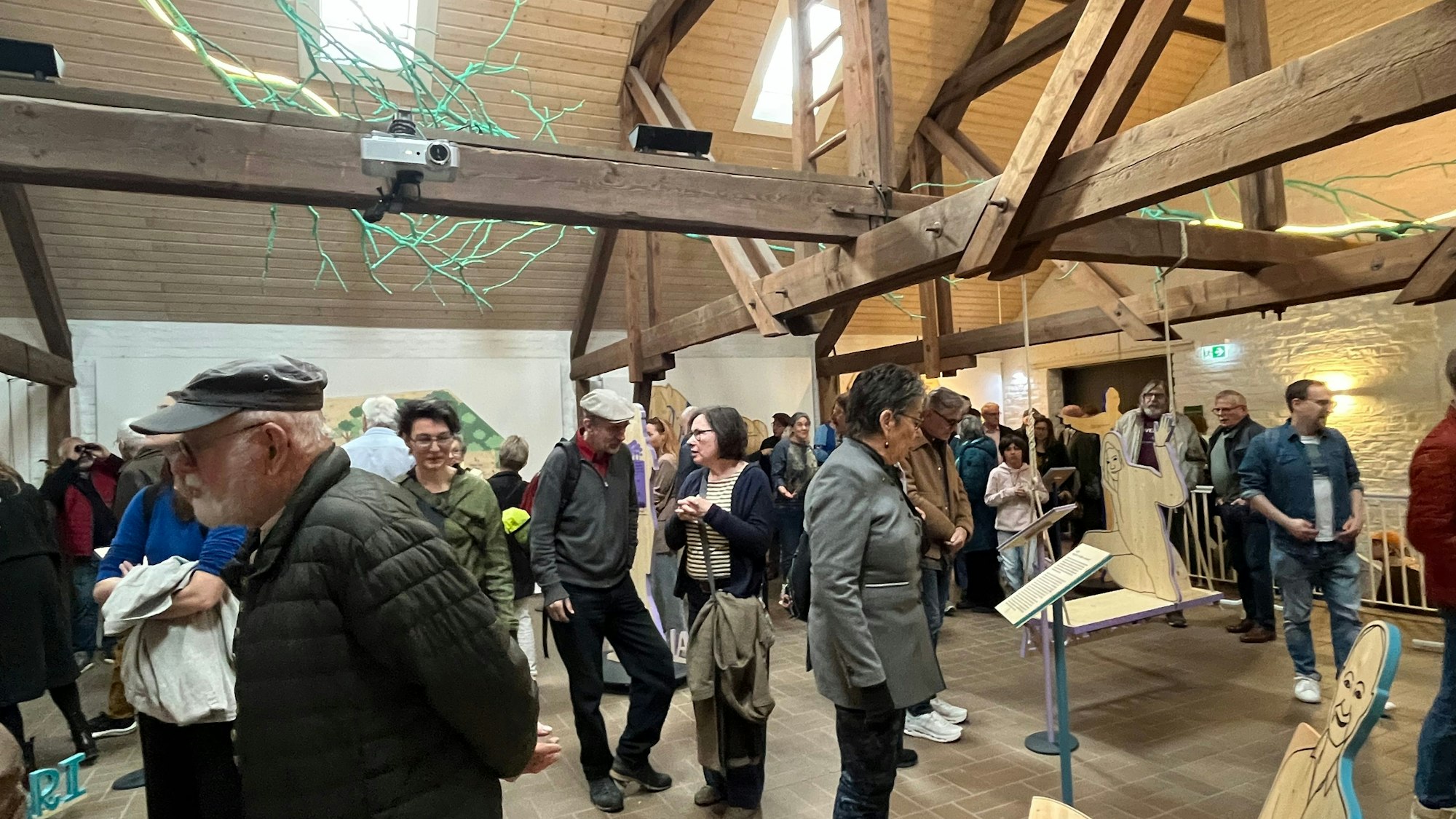 Viele Menschen stehen in einem großen Raum mit Ausstellungsstücken aus Holz.