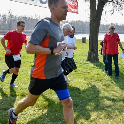 Zu sehen sind mehrere Läufer auf Rasen an einem See.