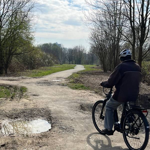 Ein Radfahrer fährt über einen Weg, an dem eine tiefe Pfütze entstanden ist.