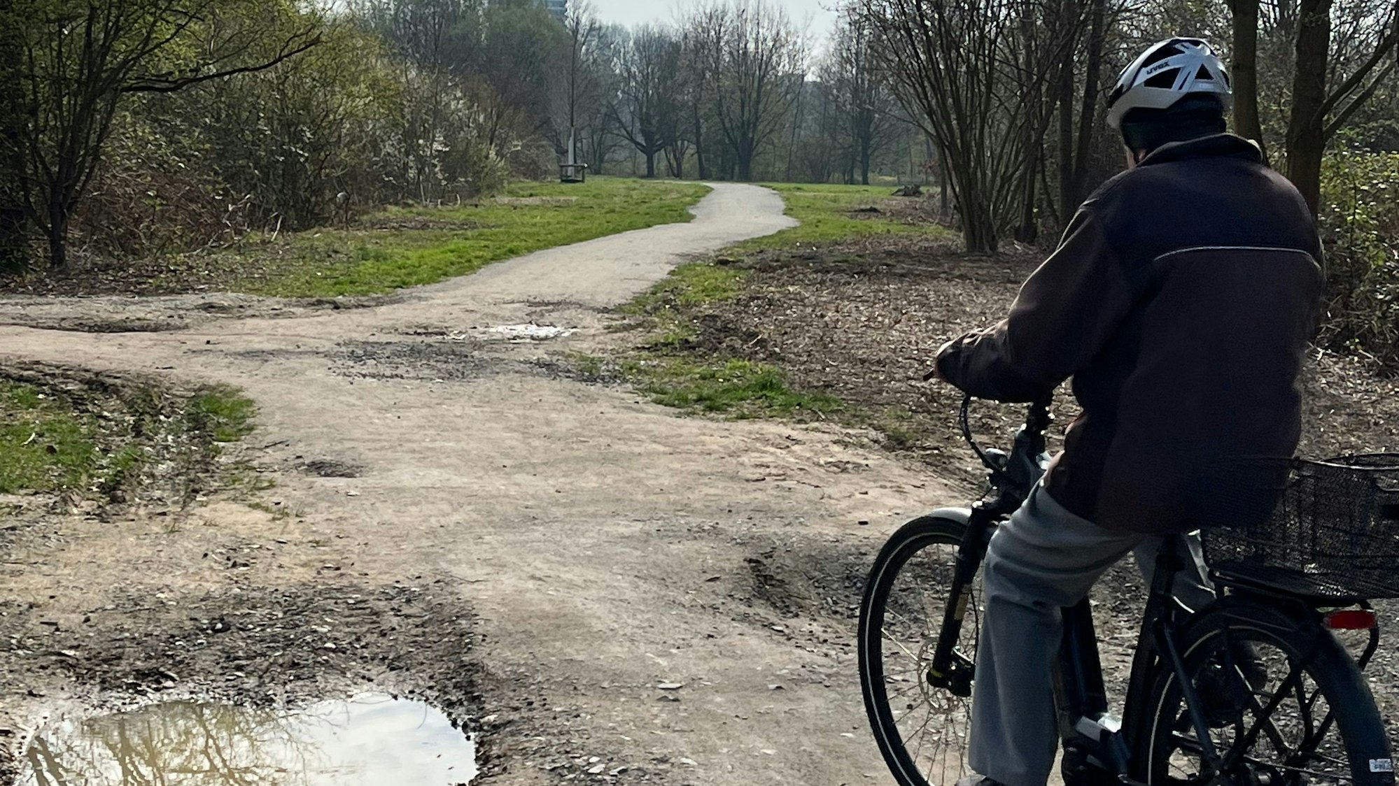 Ein Radfahrer fährt über einen Weg, an dem eine tiefe Pfütze entstanden ist.
