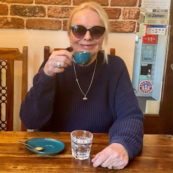 Yvonne Eckhardt sitzt mit einem Kaffee in der Hand an einem Tisch.