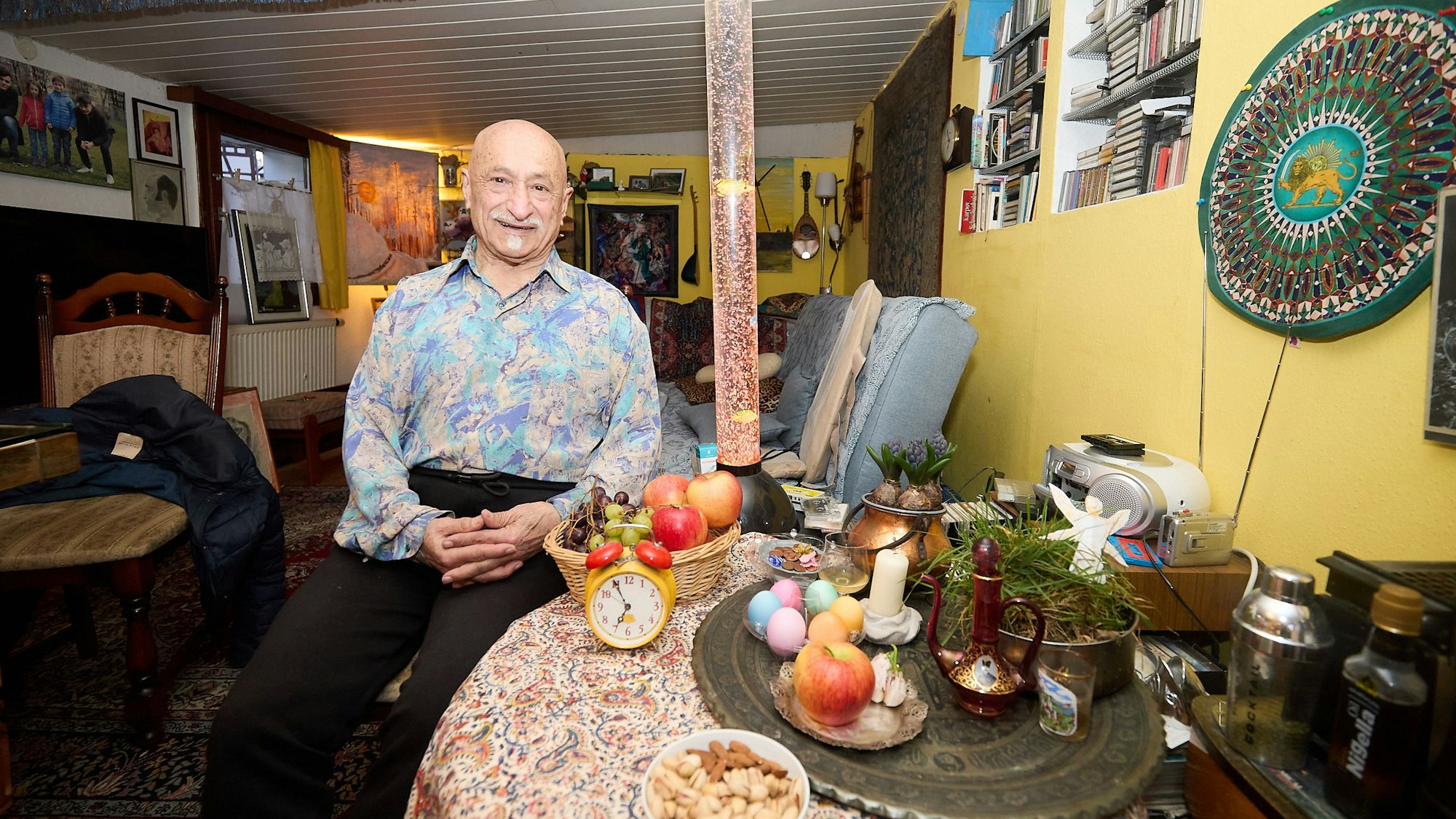 Hassan Deldjoue Shahir sitzt an einem Tisch, auf dem er Dinge arrangiert hat, die Glück und Gesundheit symbolisieren sollen.