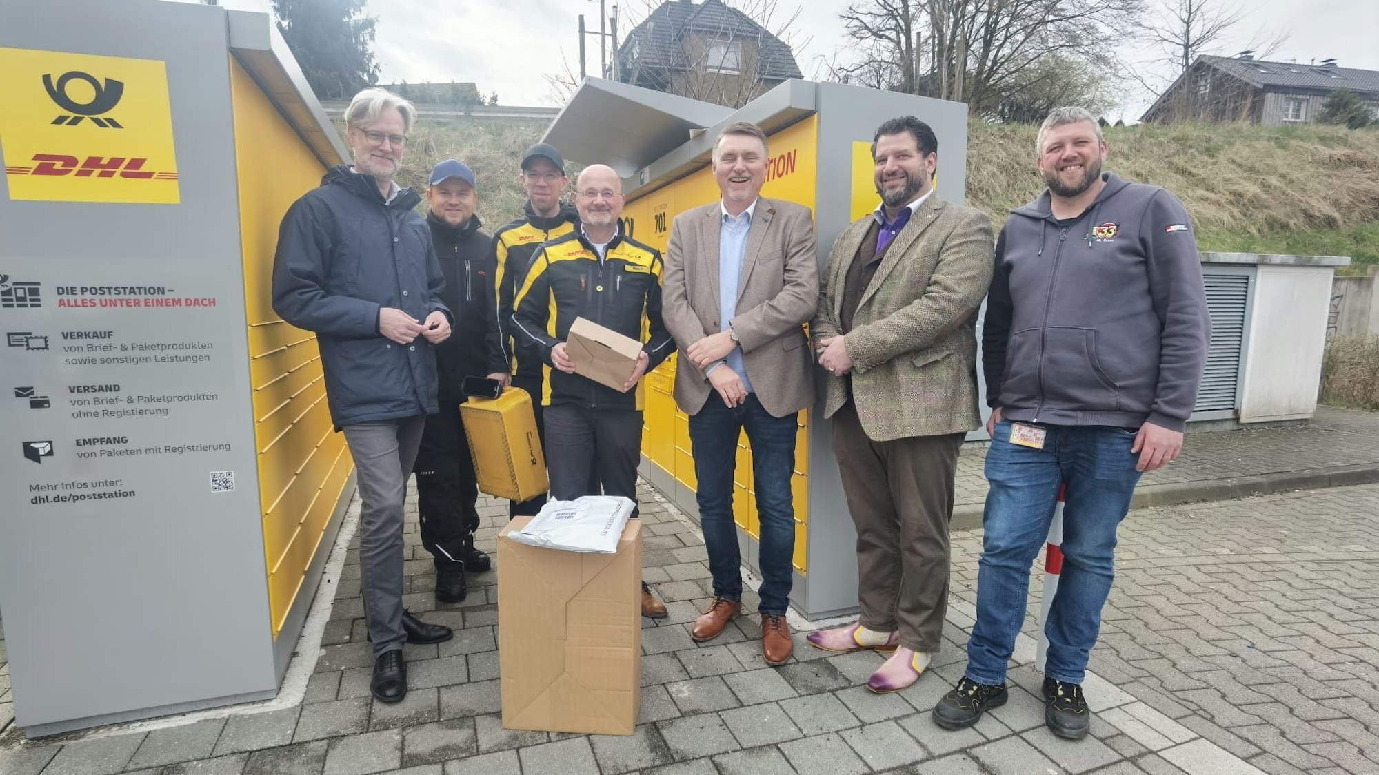 Eine Gruppe Männer steht vor einer DHL/Deutsche Post Packstation.