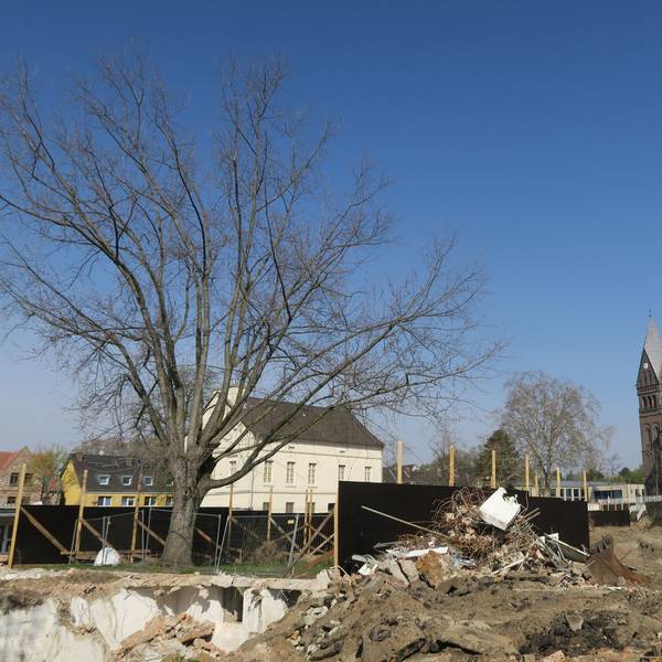 Vor einem alten Gutshaus und einer Kirche erstreckt sich ein großes Areal, auf dem Abbruchspuren zu sehen sind.