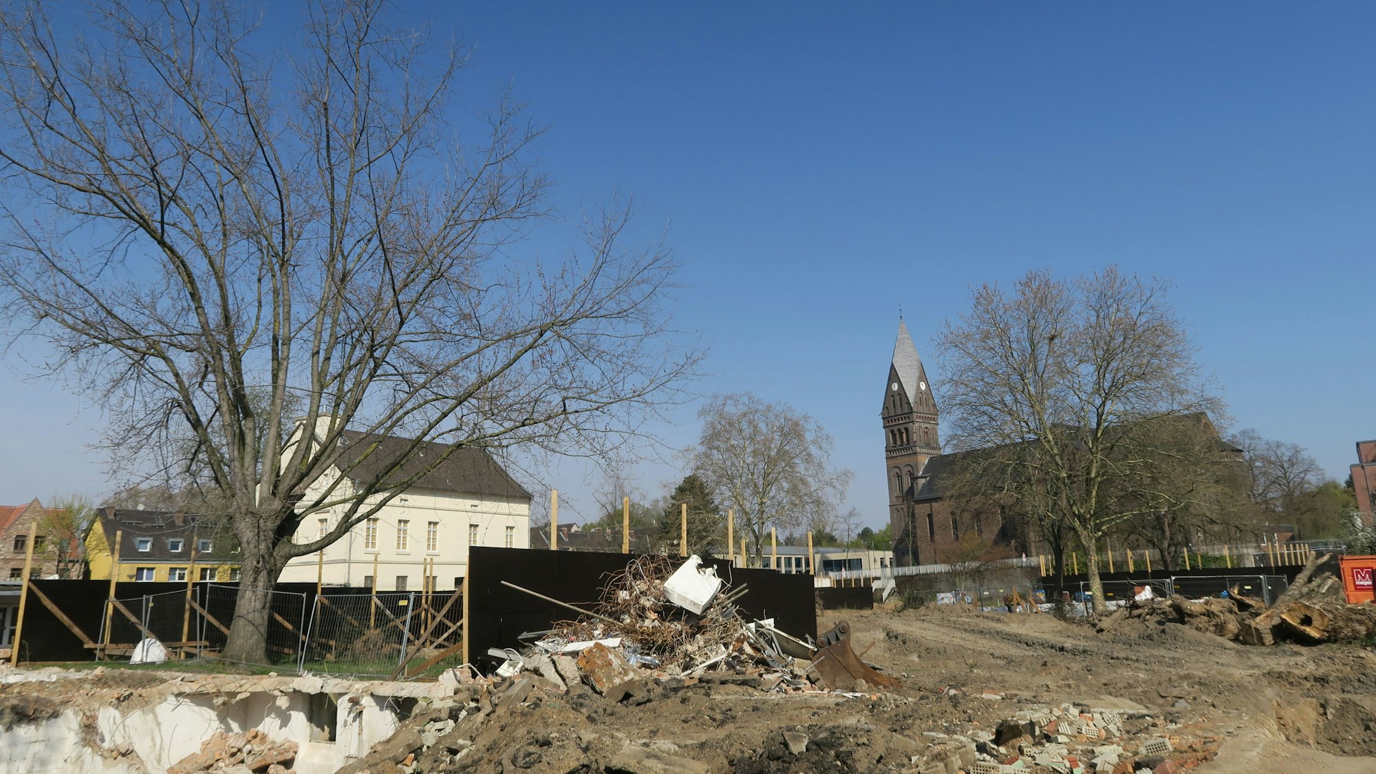Vor einem alten Gutshaus und einer Kirche erstreckt sich ein großes Areal, auf dem Abbruchspuren zu sehen sind.