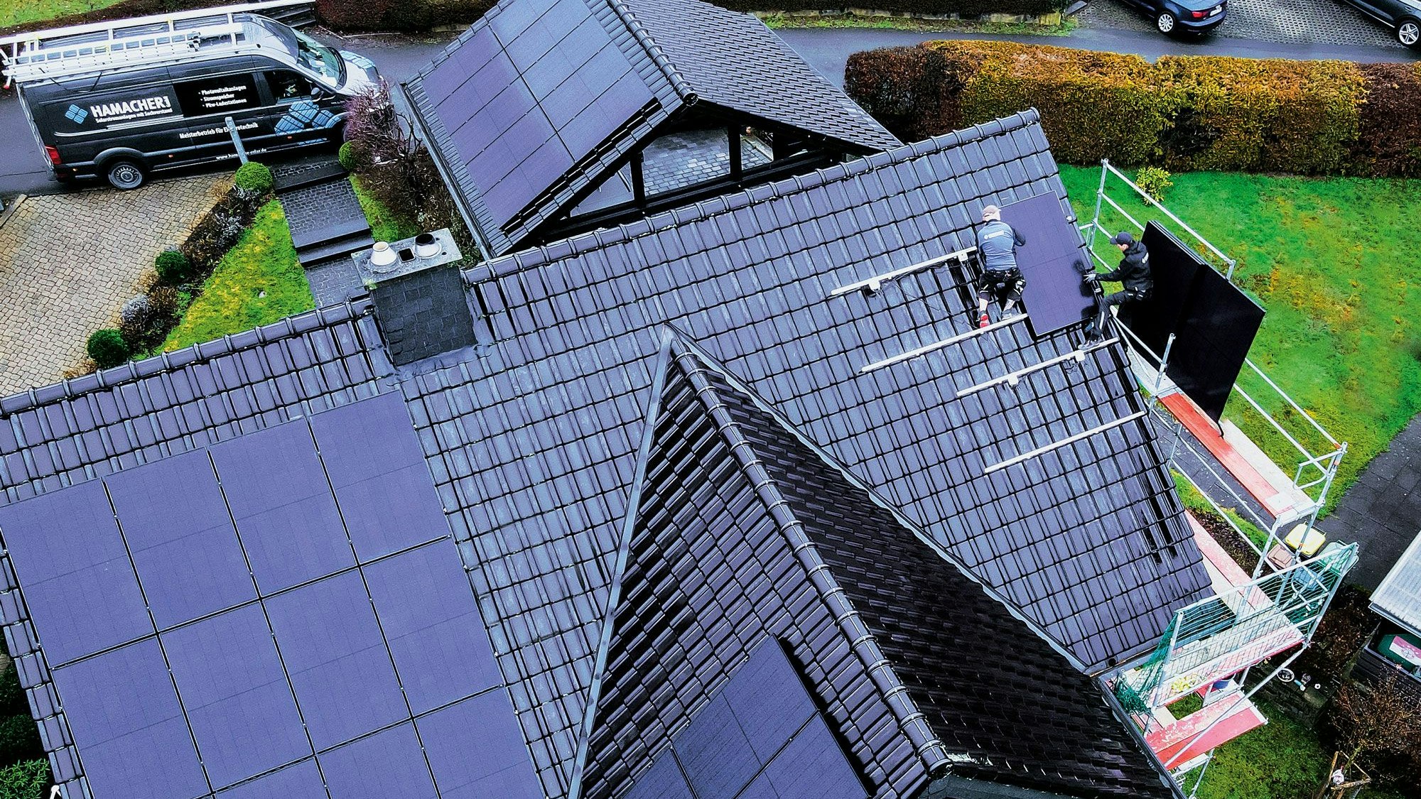 Luftbildaufnahme auf ein dunkles Dach, das mit Solarpanelen gedeckt wird.