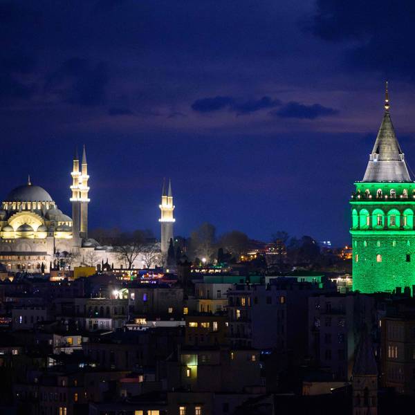 Grün angestrahlter Galata-Turm mit Moschee im Hintergrund bei Nacht.