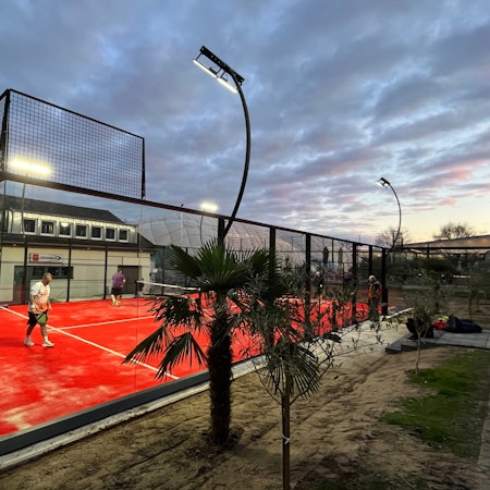 Eine Art Mini-Tennisplatz mit Glaswänden steht vor einem Vereinsheim.