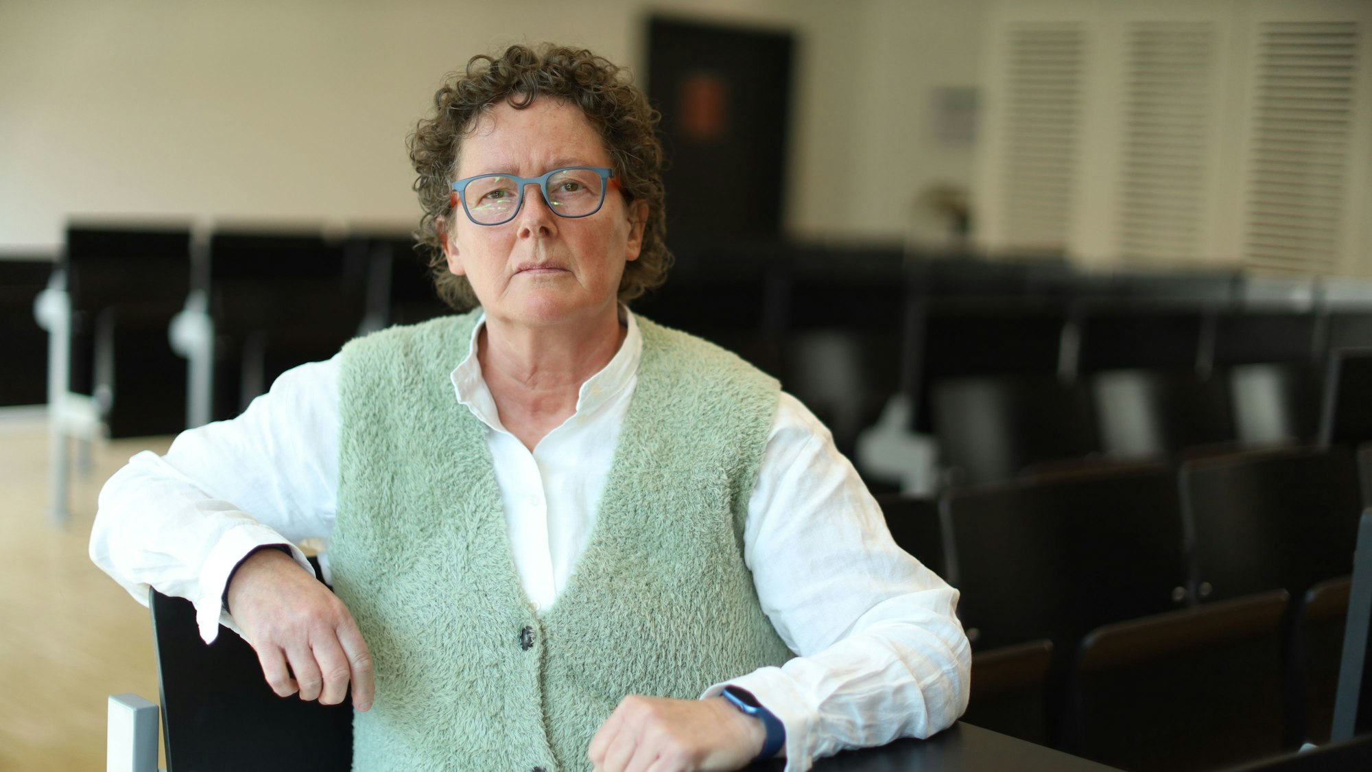 Eine Frau mit grüner Weste schaut ernst in die Kamera.