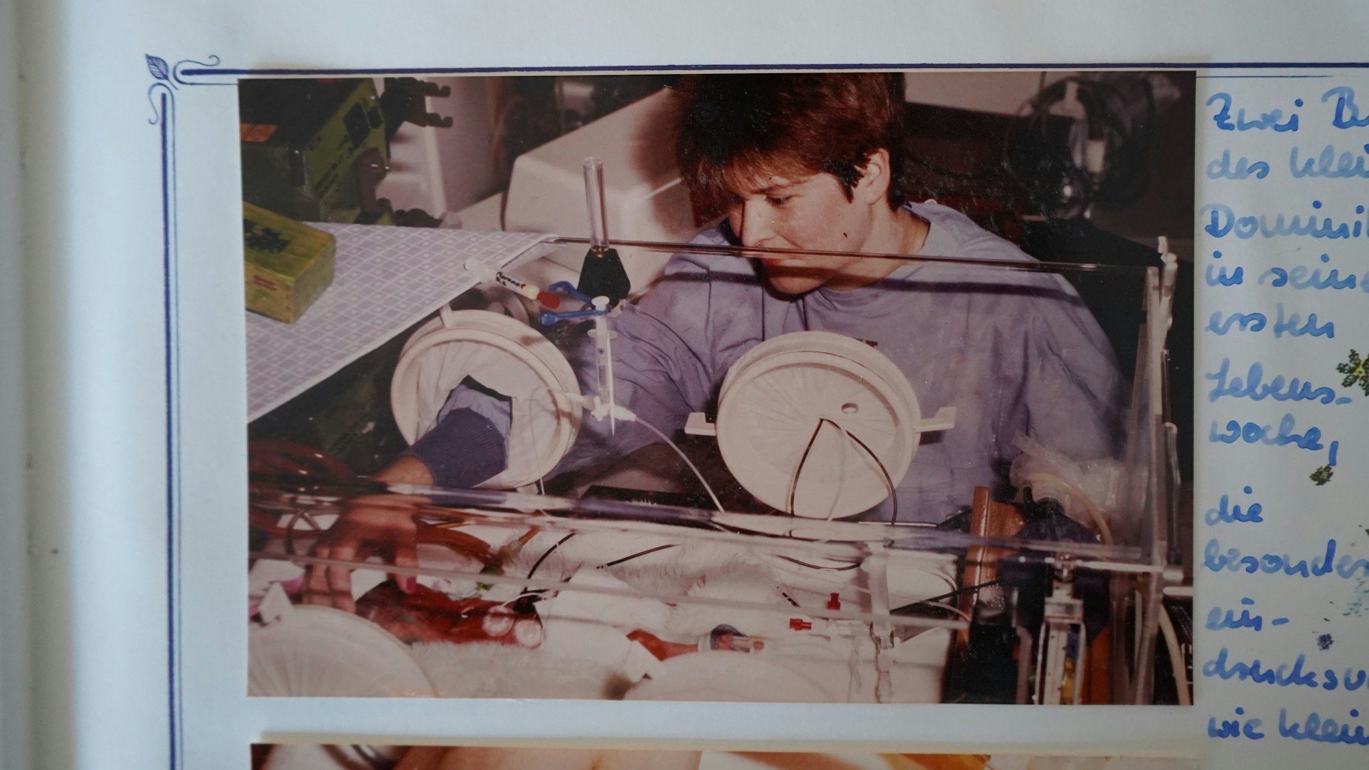 Das Bild zeigt ein Foto im Babyalbum. Claudia holzgartner sitzt neben einem Brutkasten und streichelt durch die Öffnung hindurch sanft einen ihrer fünf Söhne den Kopf.