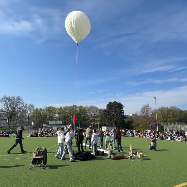 Jugendliche stehen auf einem Sportplatz um einen weißen Ballon herum.
