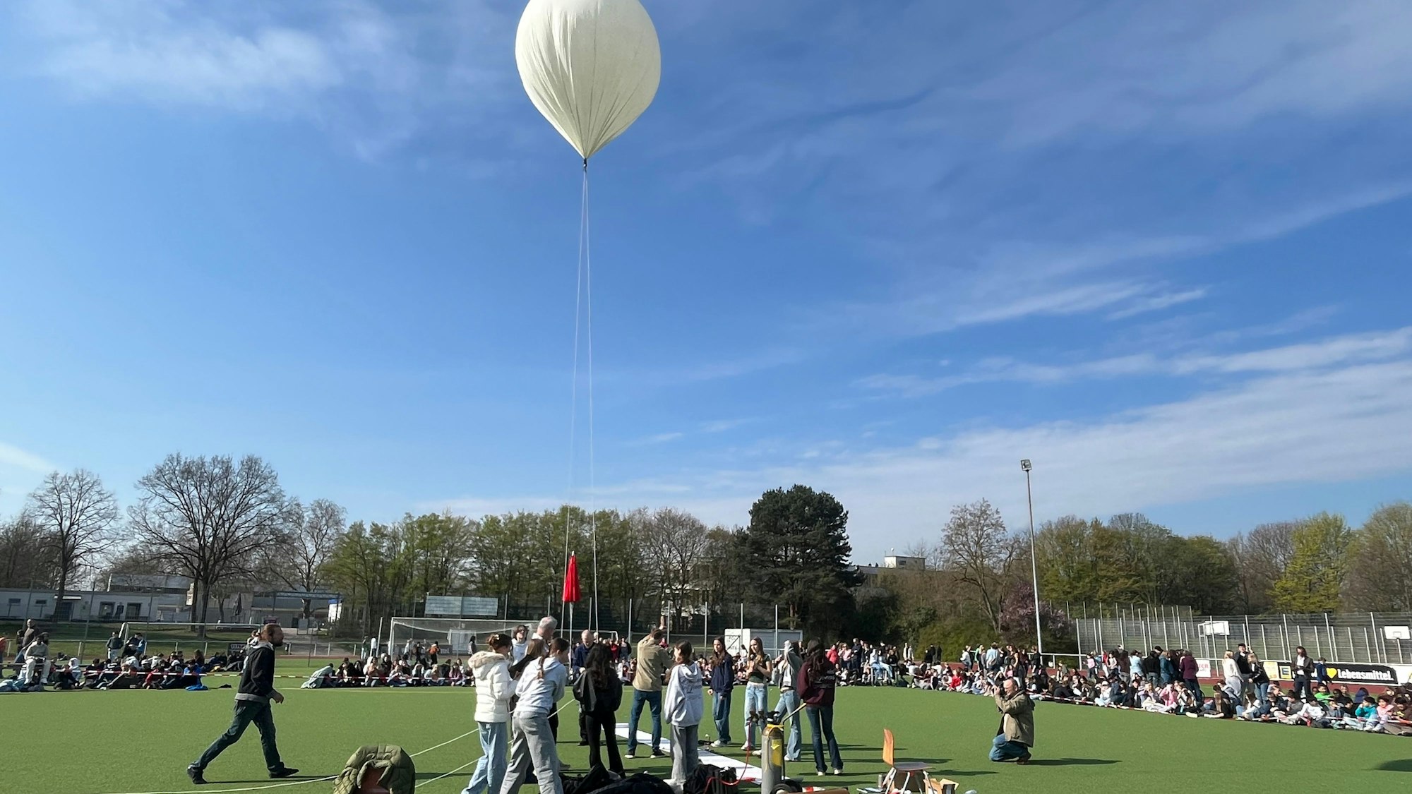 Jugendliche stehen auf einem Sportplatz um einen weißen Ballon herum.