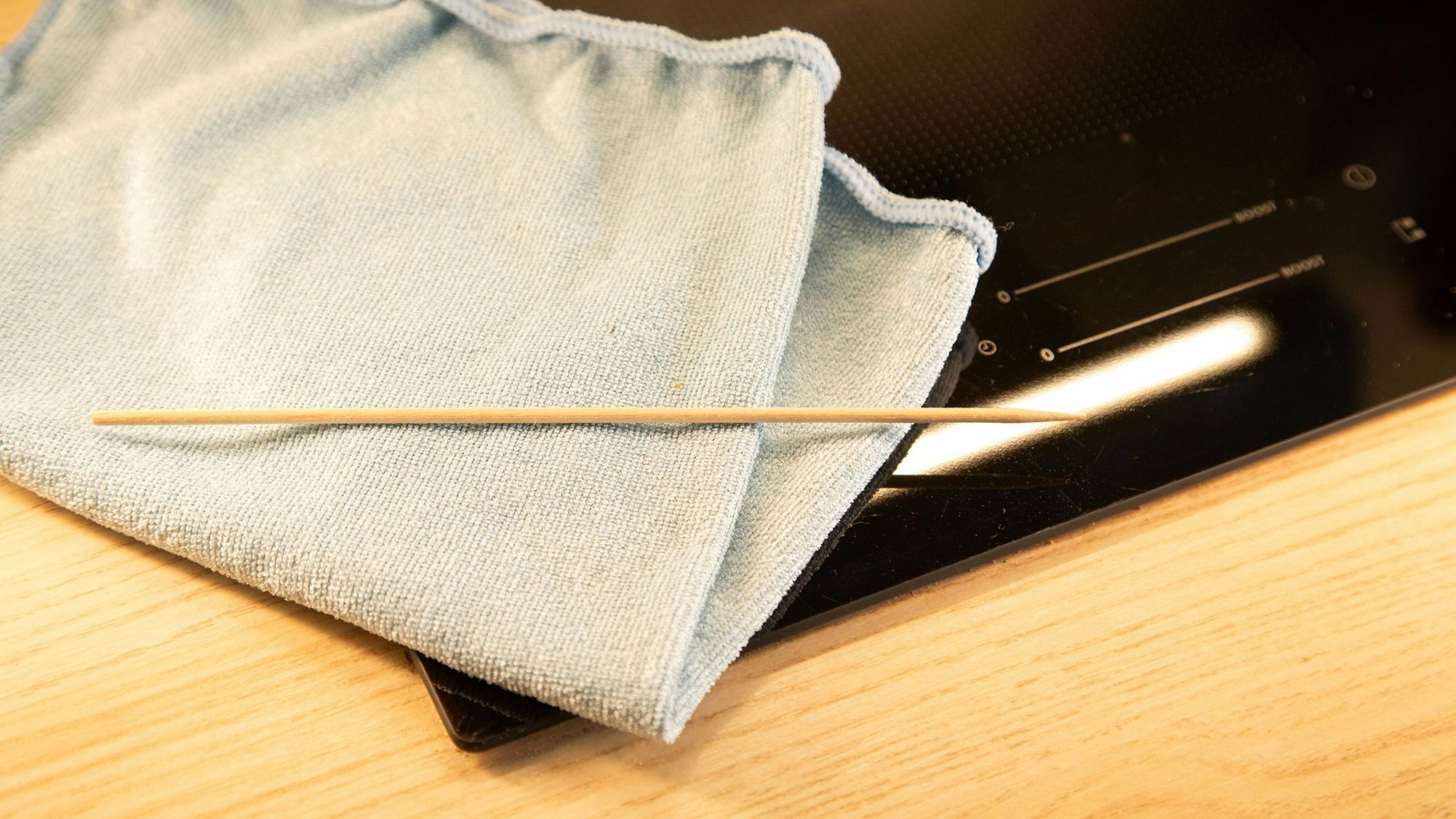 Ein Holzspieß und ein Mikrofasertuch liegen neben einem Kochfeld