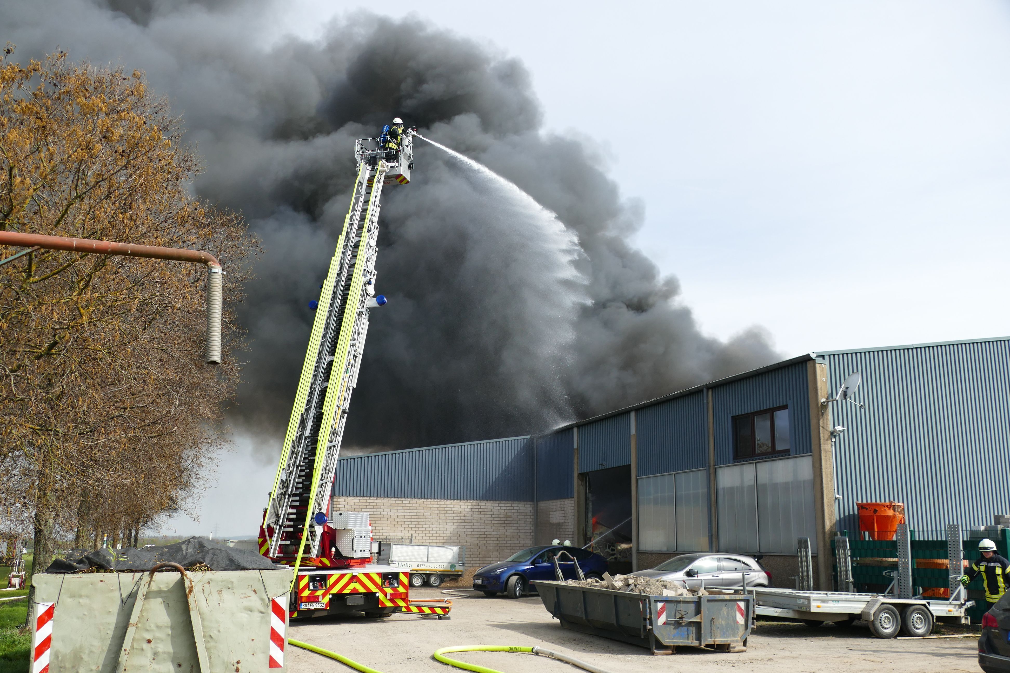 Drehleiter der Feuerwehr im Einsatz über einer brennenden Lagerhalle.