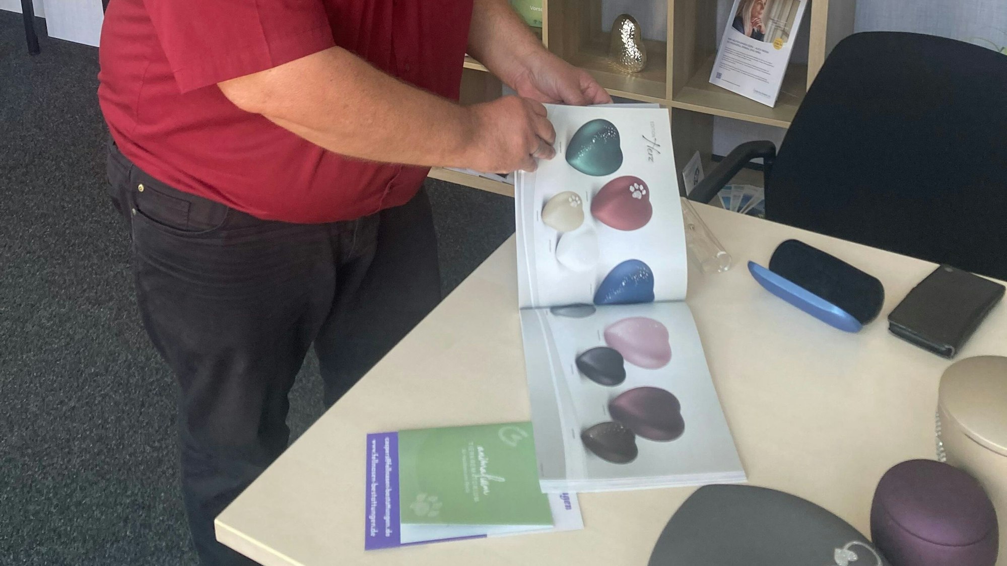 Das Bild zeigt einen Mitarbeiter beim Durchblättern eines Katalogs mit Urnen.