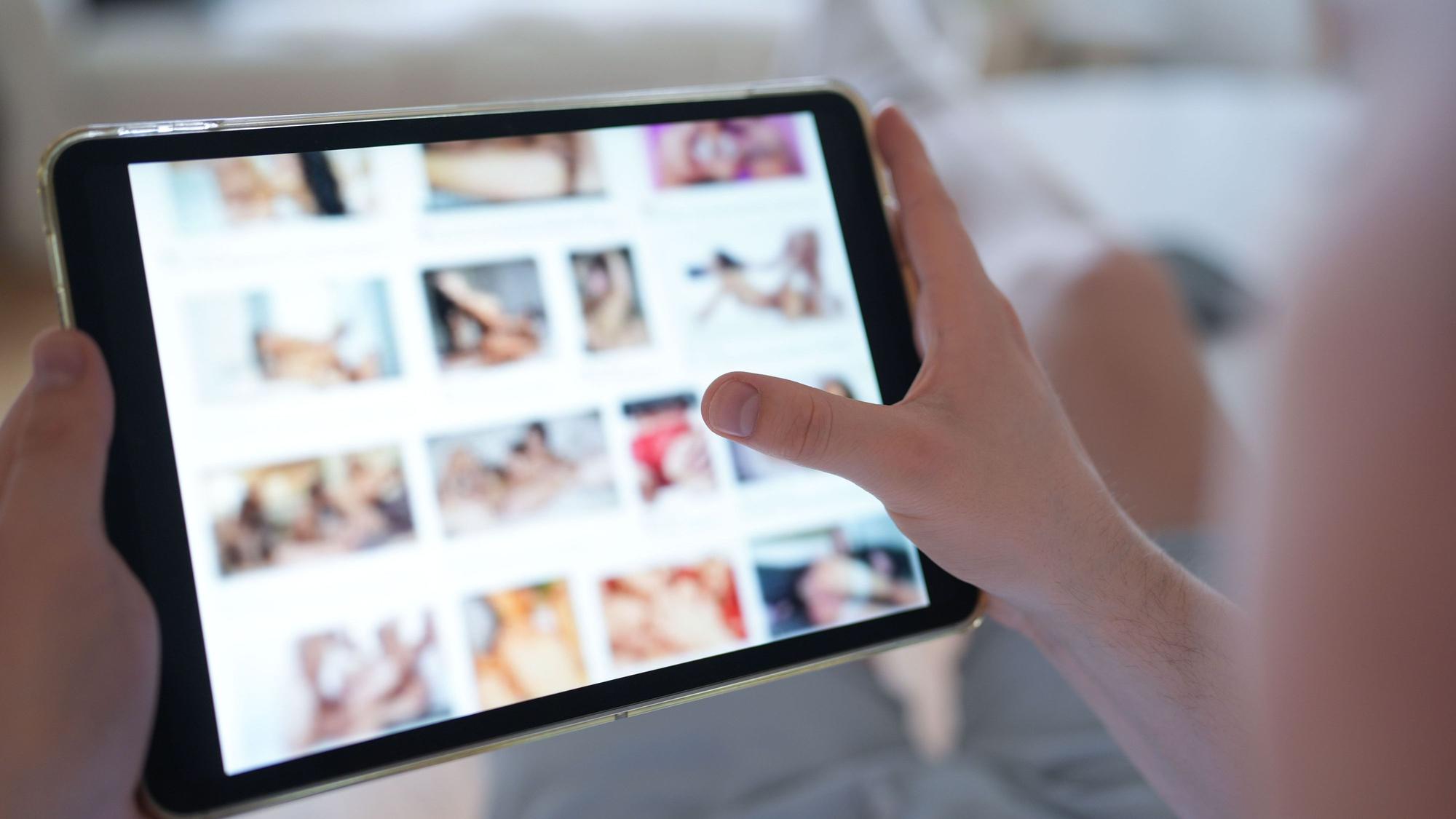 Ein junger Mann schaut sich auf einem Smartphone eine Porno-Internetseite an (gestellte Szene).