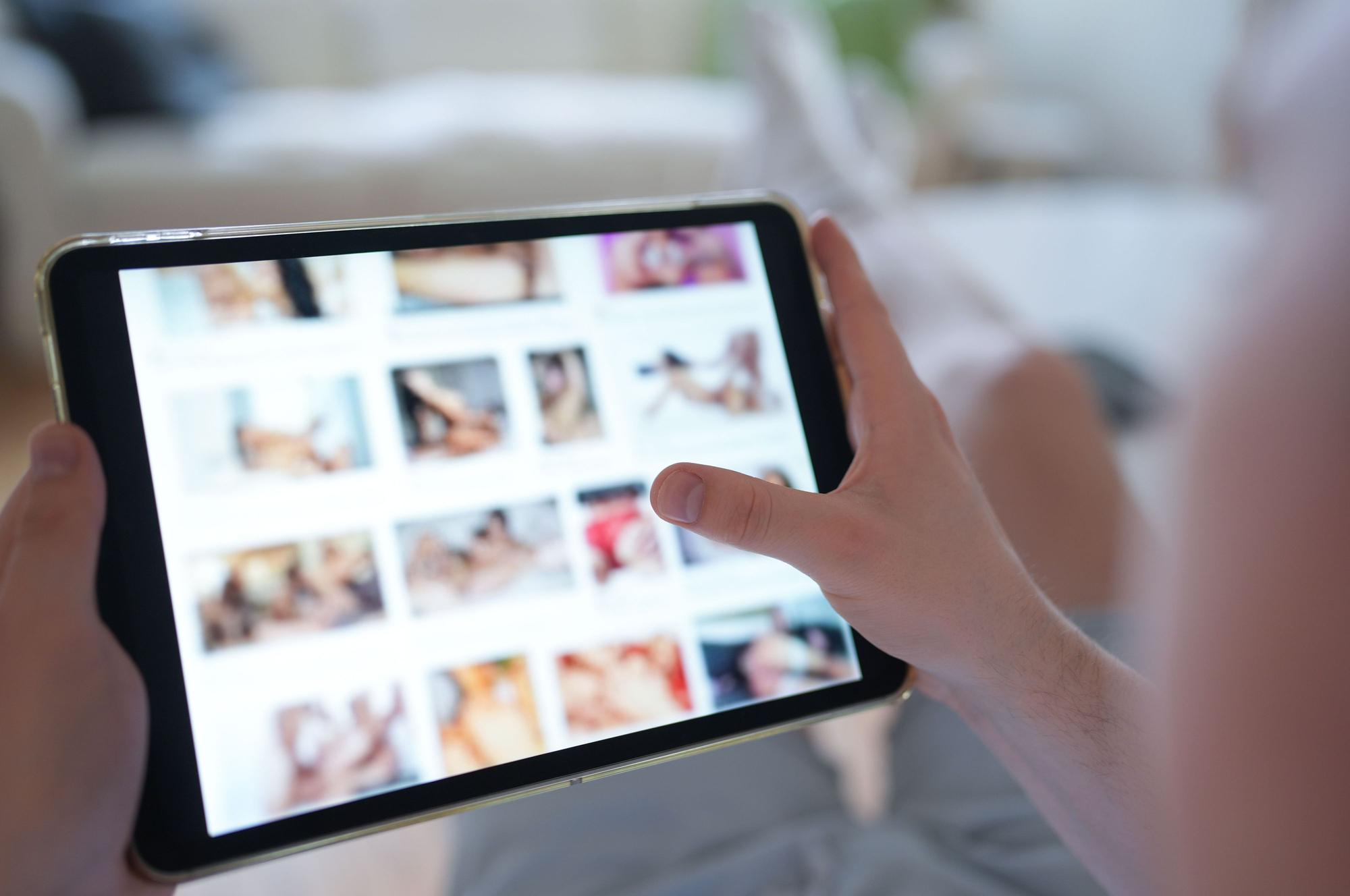Ein junger Mann schaut sich auf einem Smartphone eine Porno-Internetseite an (gestellte Szene).