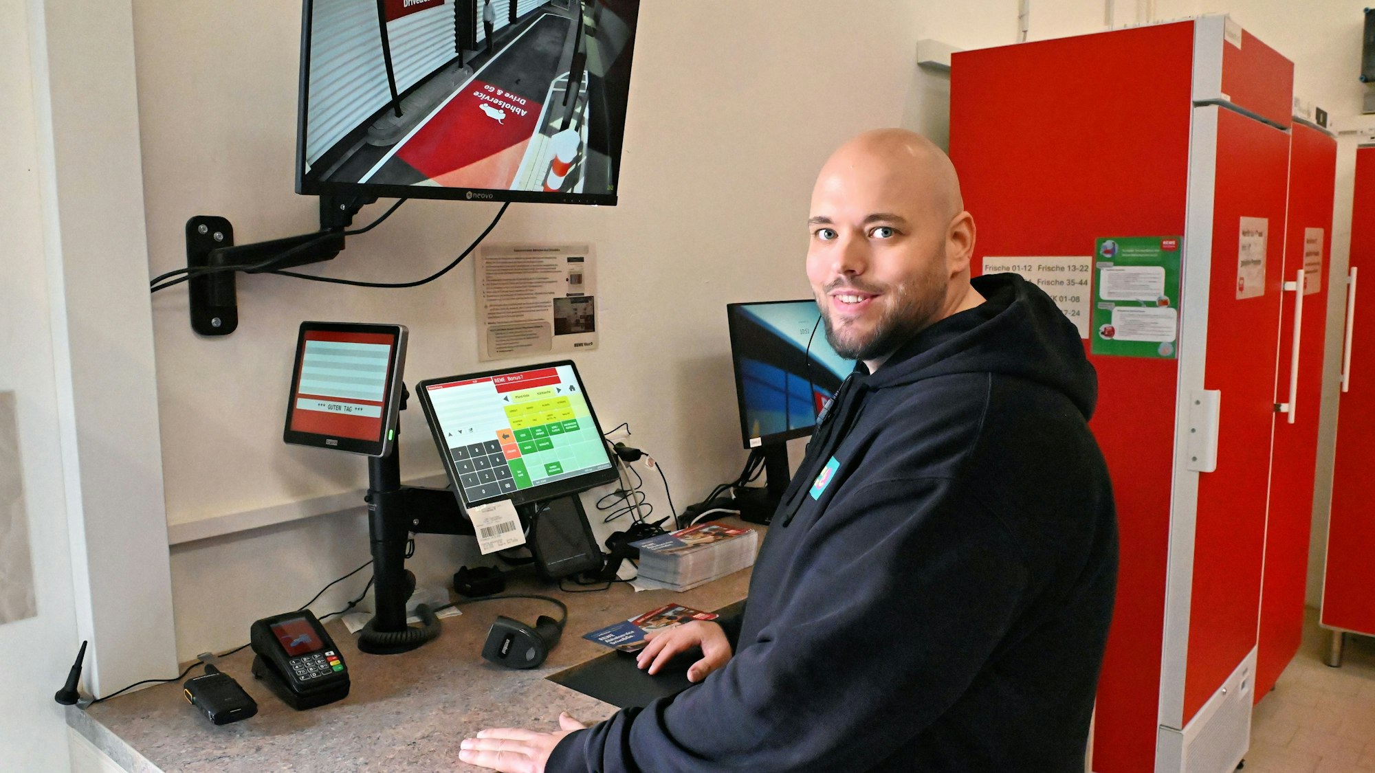Rewe-Mitarbeiter Stephan Steinebach sitzt an einem Tisch mit mehreren Bildschirmen.