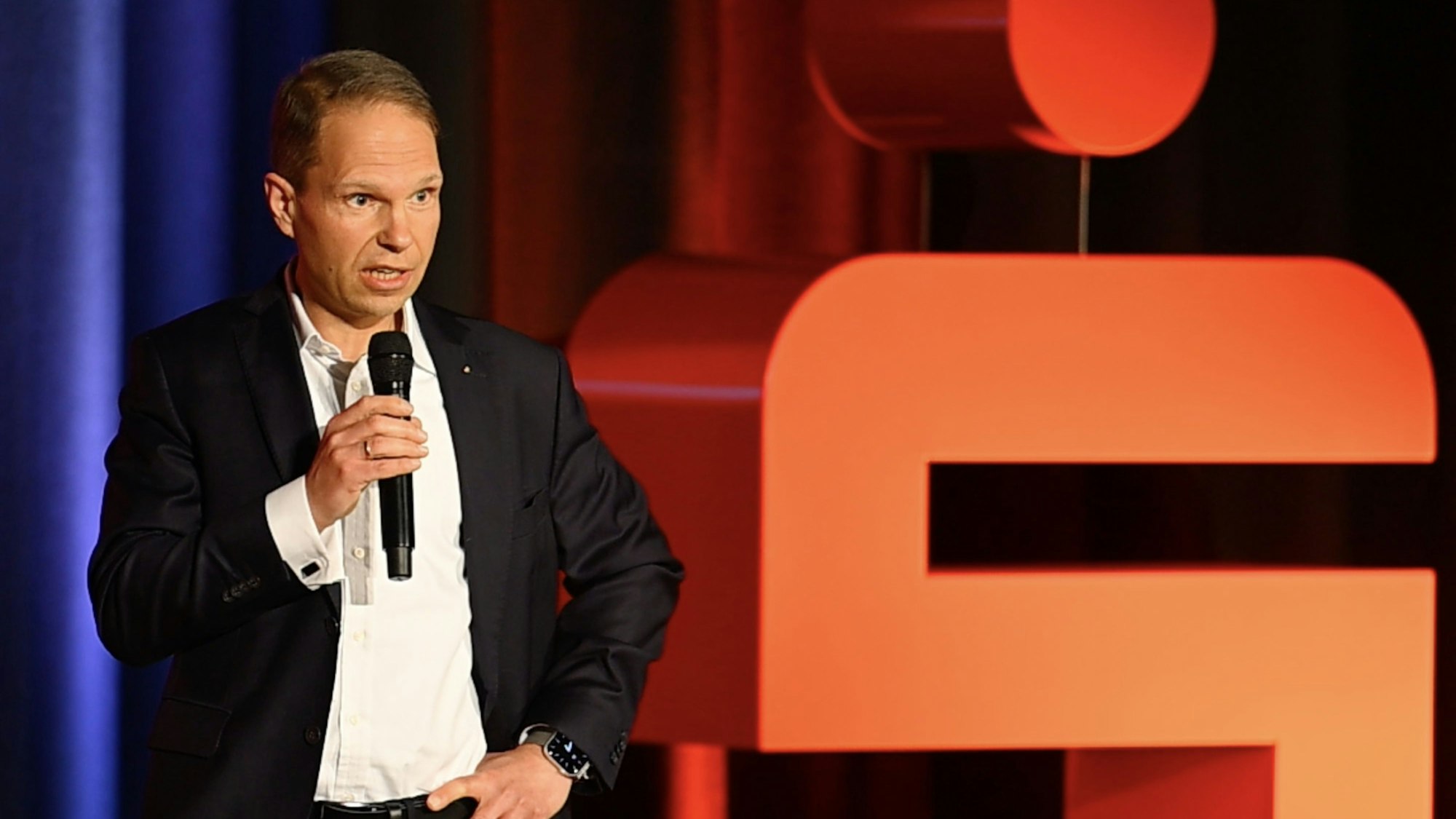 Zu sehen ist ein Bankvorstand mit Mikrofon