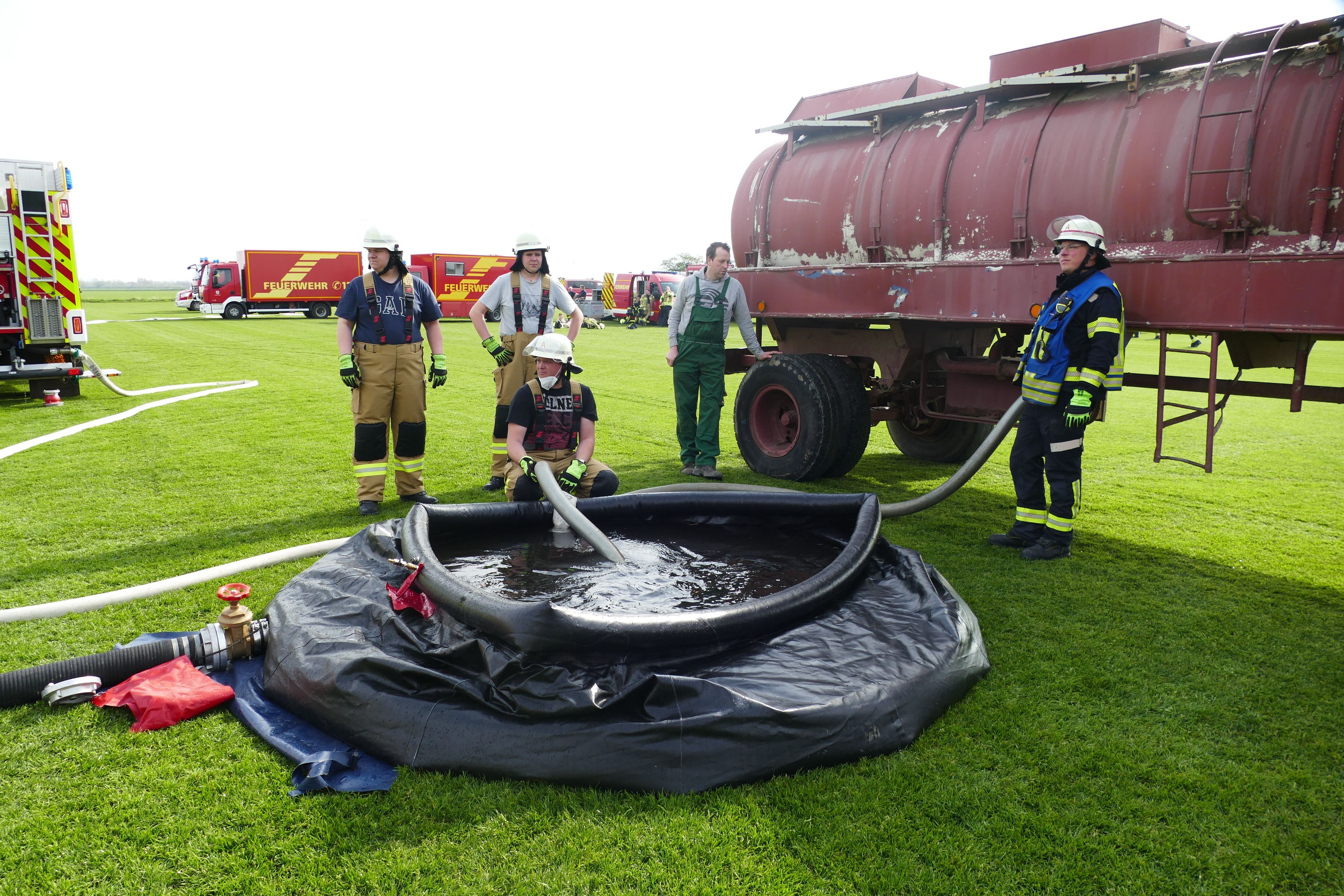 Feuerwehrleute füllen ein schwarzes Schlauchbecken mit Wasser aus einem Güllelaster.