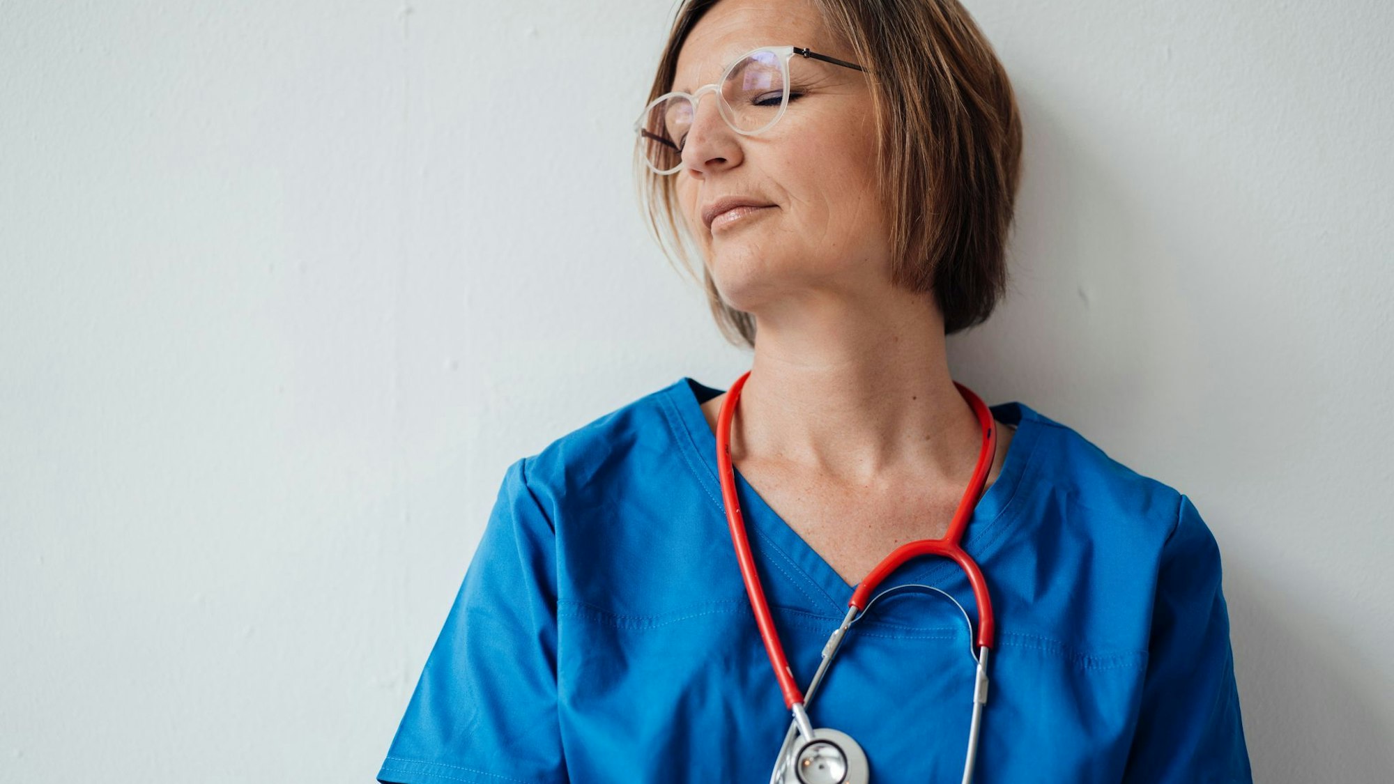 Eine Ärztin lehnt mit geschlossenen Augen an der Wand