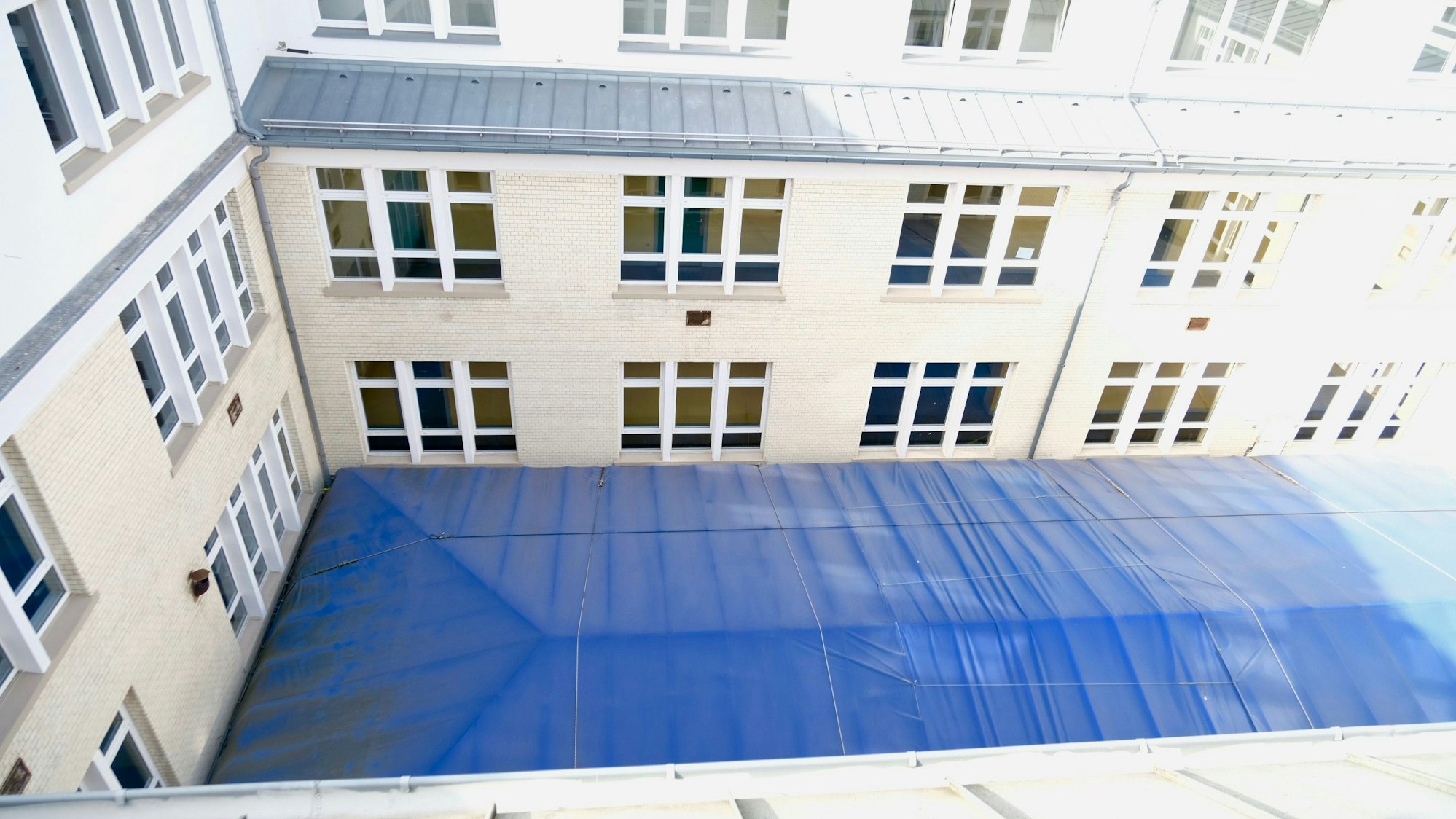In einem Innenhof ist eine blaue Plane gespannt.