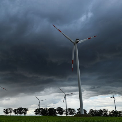 Zu sehen sind dunkle Wolken am Himmel über mehreren Windrädern