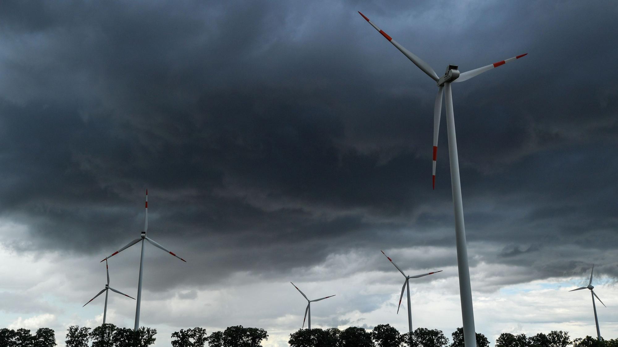 Zu sehen sind dunkle Wolken am Himmel über mehreren Windrädern