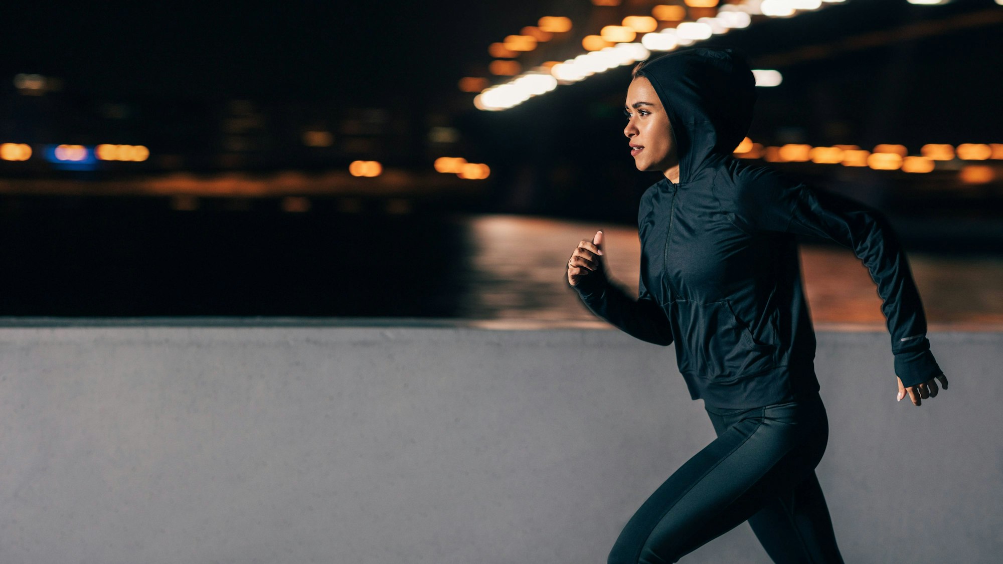 Seitenansicht einer Frau im Kapuzenpulli beim Nachtlauf.