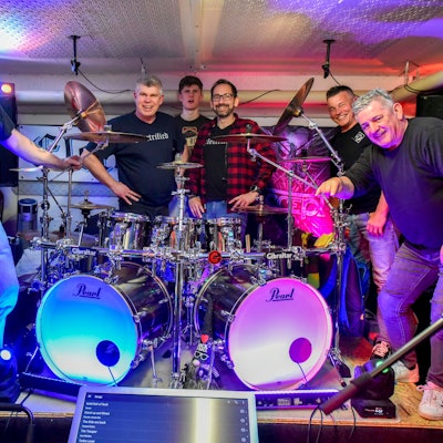 Auf dem Bild sind die Musiker der Frechener Band Electrified zu sehen, die im Proberaum um ein Schlagzeug versammelt sind.