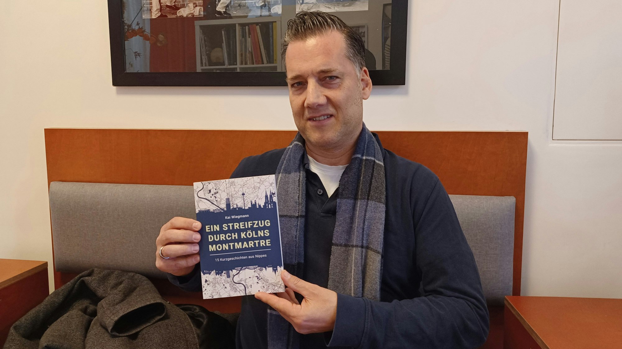 Ein Mann hält ein Kurzgeschichten-Buch mit dem Titel Ein Streifzug durch Kölns Montmartre in den Händen.