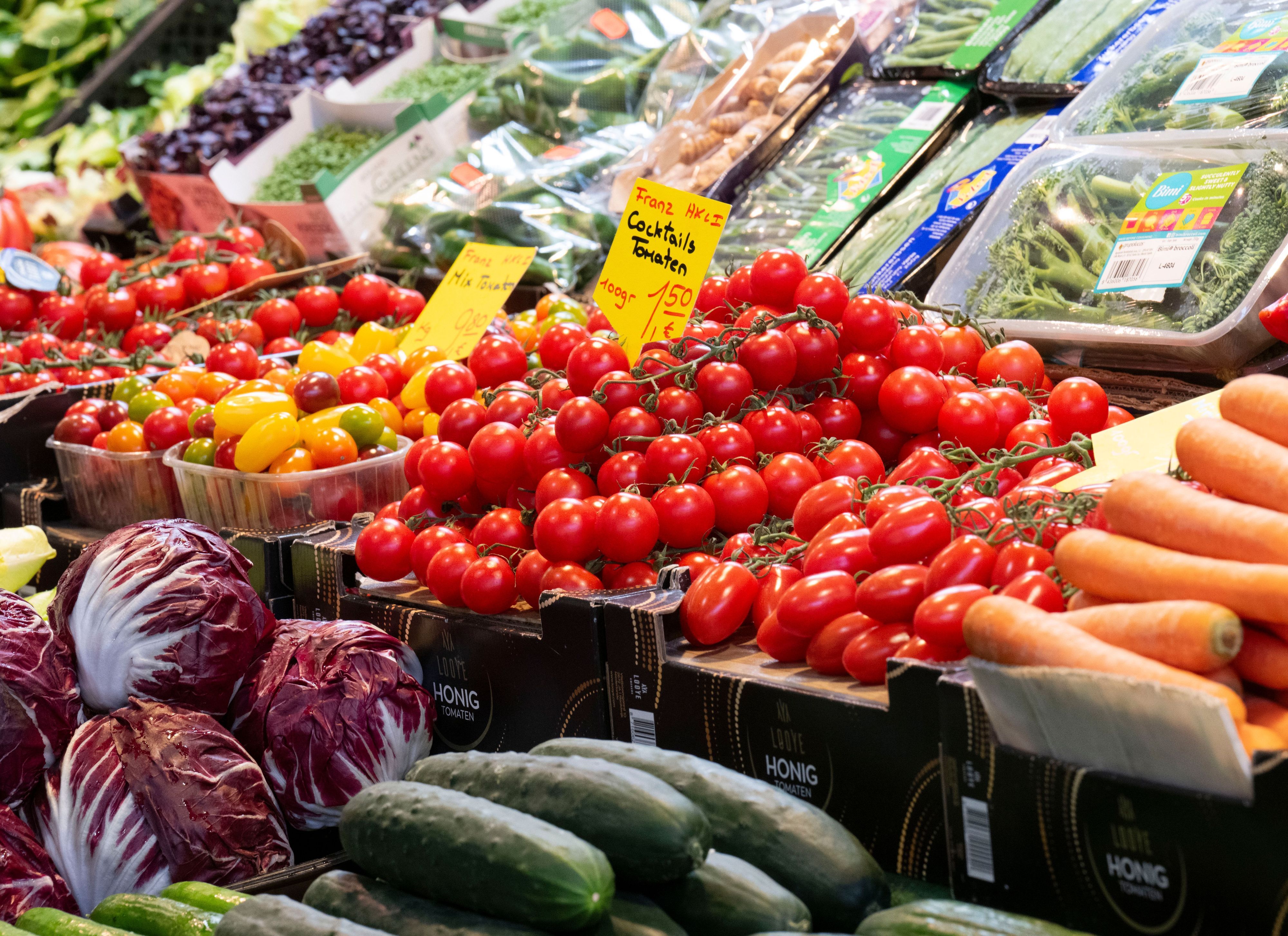 Gemüse wie Tomaten liegt in den Auslagen eines Marktstandes und ist mit Preisschildern ausgezeichnet.