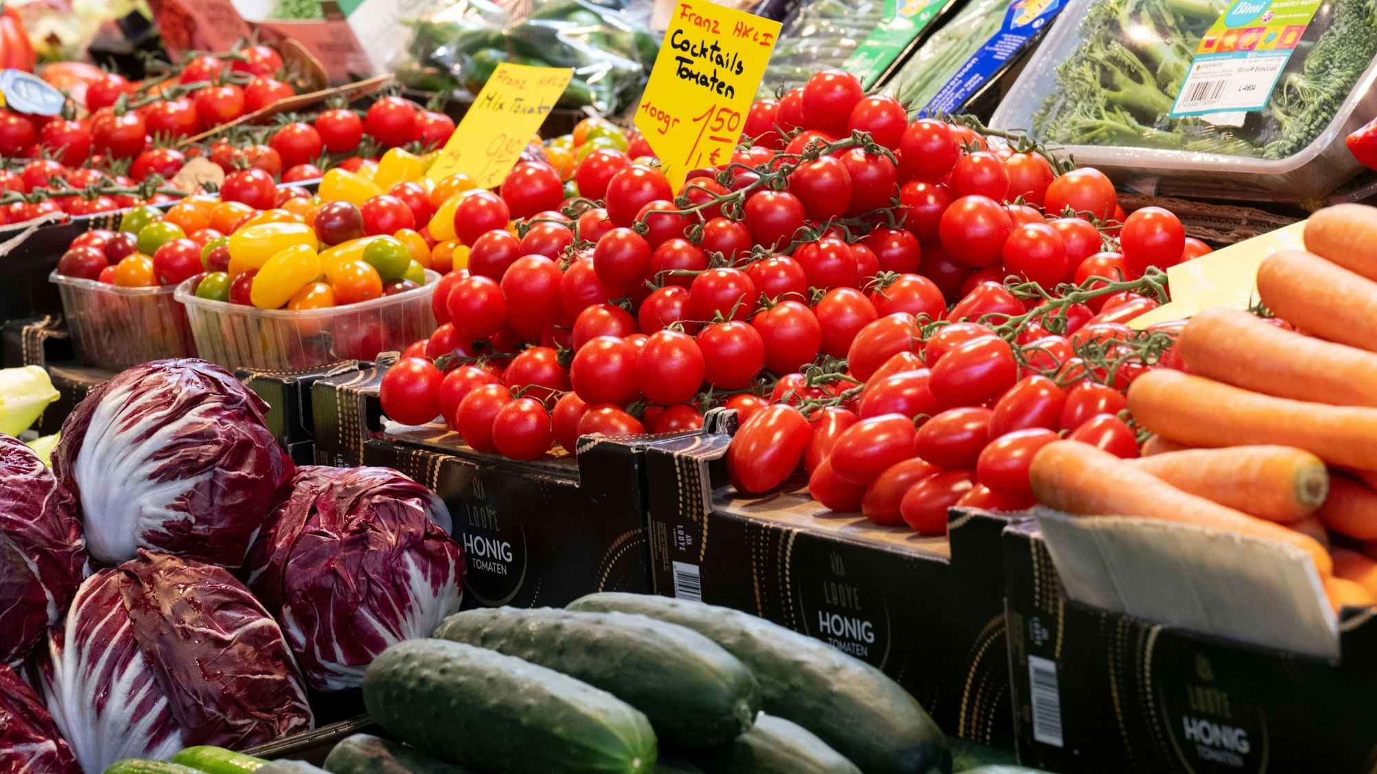 Gemüse wie Tomaten liegt in den Auslagen eines Marktstandes und ist mit Preisschildern ausgezeichnet.