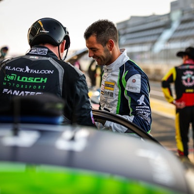 Tobias Müller unterhält sich mit einem anderen Teammitglied in der Boxengasse. Im Hintergrund steht jemand in Rennoverall und Cowboyhut.