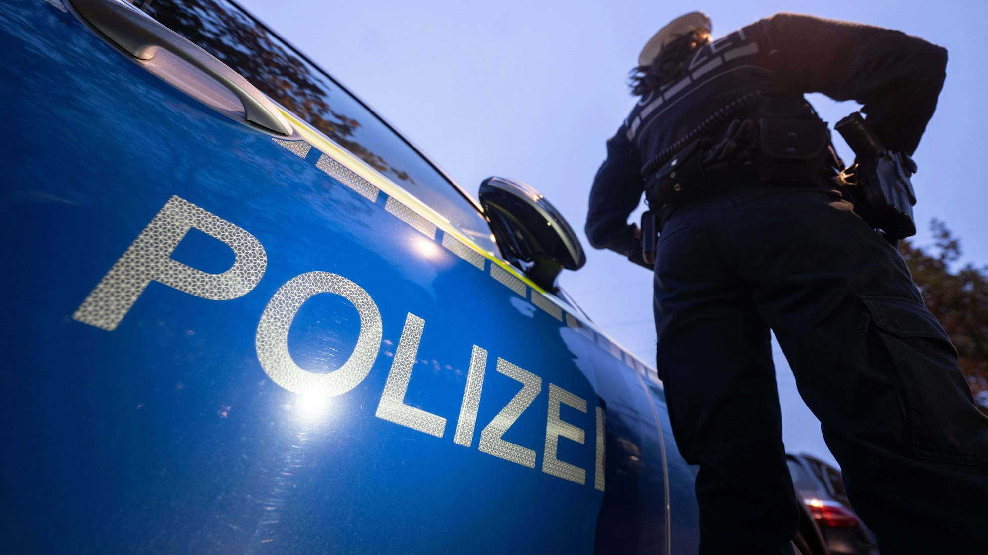 IEine Polizistin steht neben einem Polizeifahrzeug.
