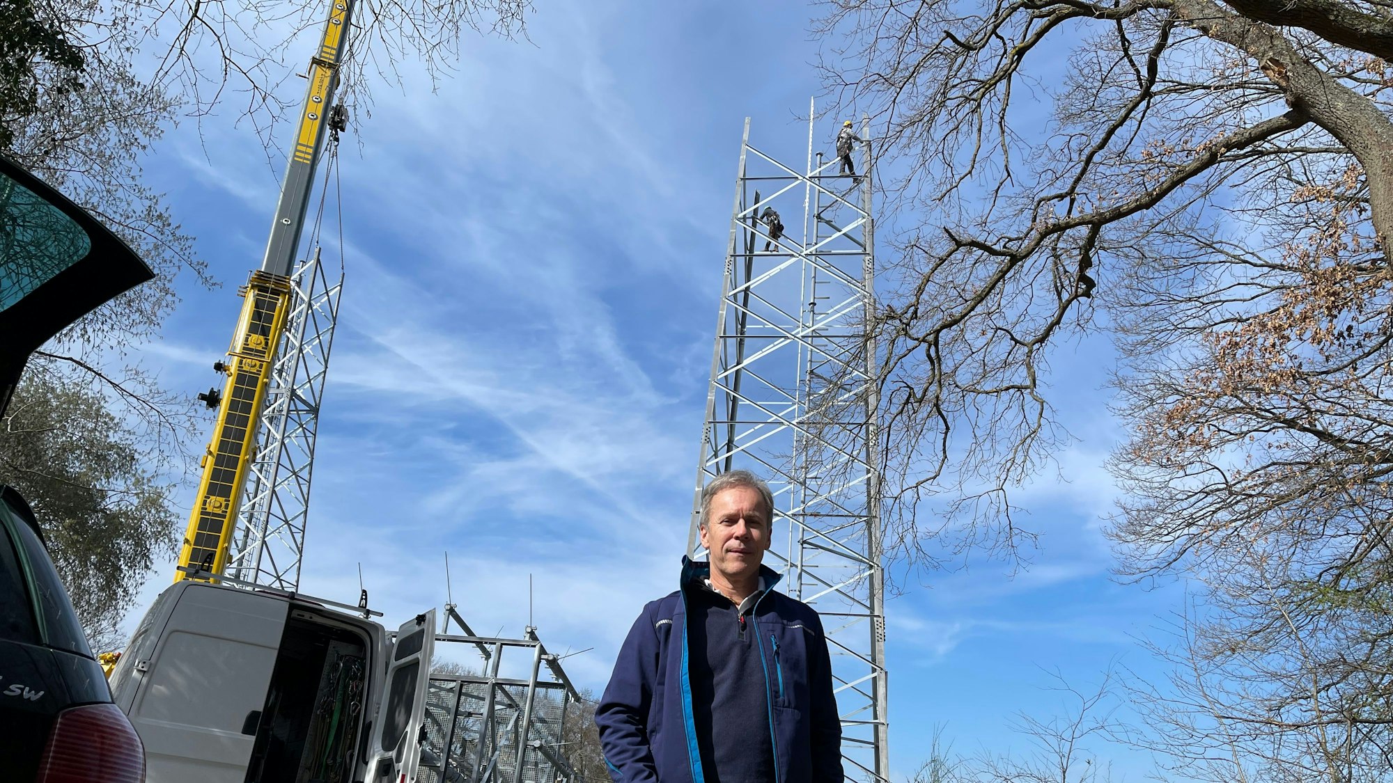 Ein Mann steht in blauer Funktionskleidung vor dem Aufbau eines Sendemasts.