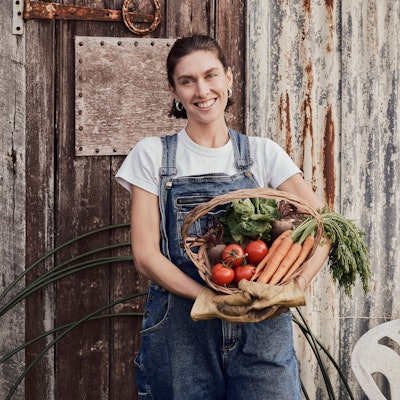 Modell einer lächelnden Frau, die im Freien sitzt und frisches Gemüse in einem Korb hält.